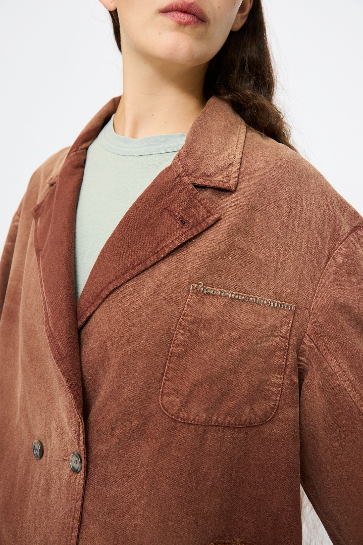 A person wearing the Dr. Collectors Bogart Jacket in Nuts, a faded brown linen-cotton blend blazer with a front pocket over a light green shirt, is shown from shoulders to chest, highlighting its vintage look.