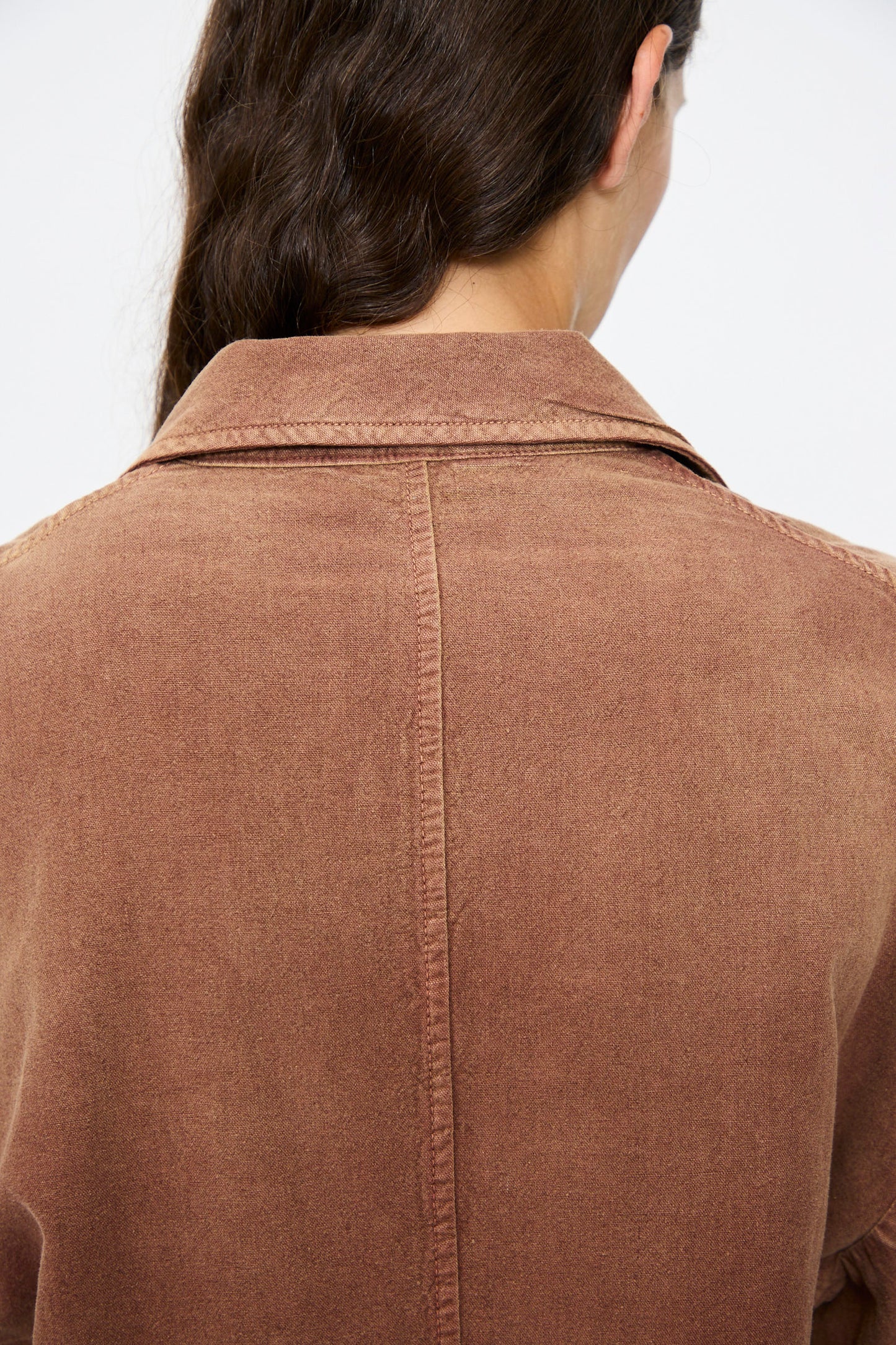 A person with long brown hair is seen from behind, wearing the Dr. Collectors Bogart Jacket in Nuts—a vintage-style brown collared jacket with visible seams down the center and shoulders.