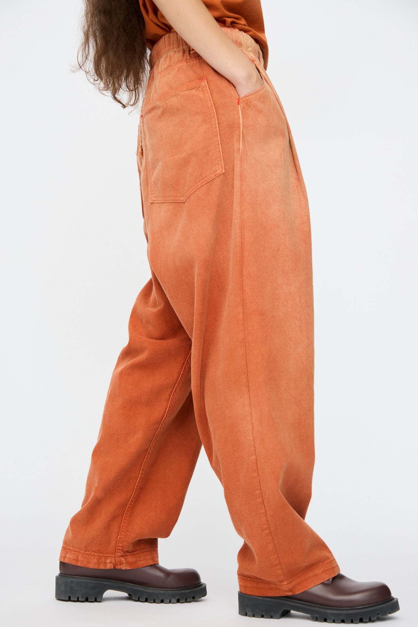 Model wears the Dr. Collectors P40 Z Boys Sunfaded Dye pants in Rust, a relaxed fit style with an elastic waistband plus side and back pockets, paired with chunky brown shoes and an orange top against a white background.