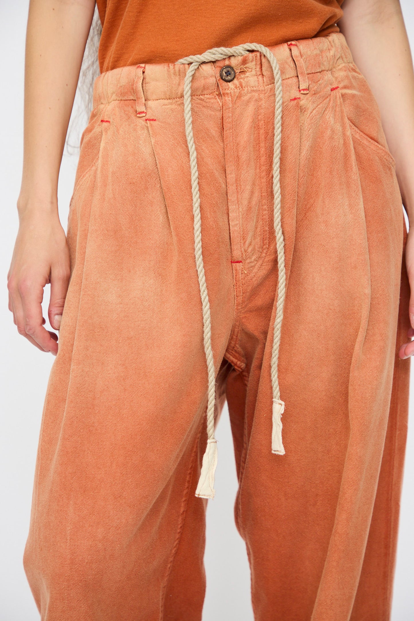 Model wearing Dr. Collectors P40 Z Boys Sunfaded Dye pants in Rust—relaxed fit Japanese cotton with a rope belt and an orange top, shown from waist to mid-thigh.