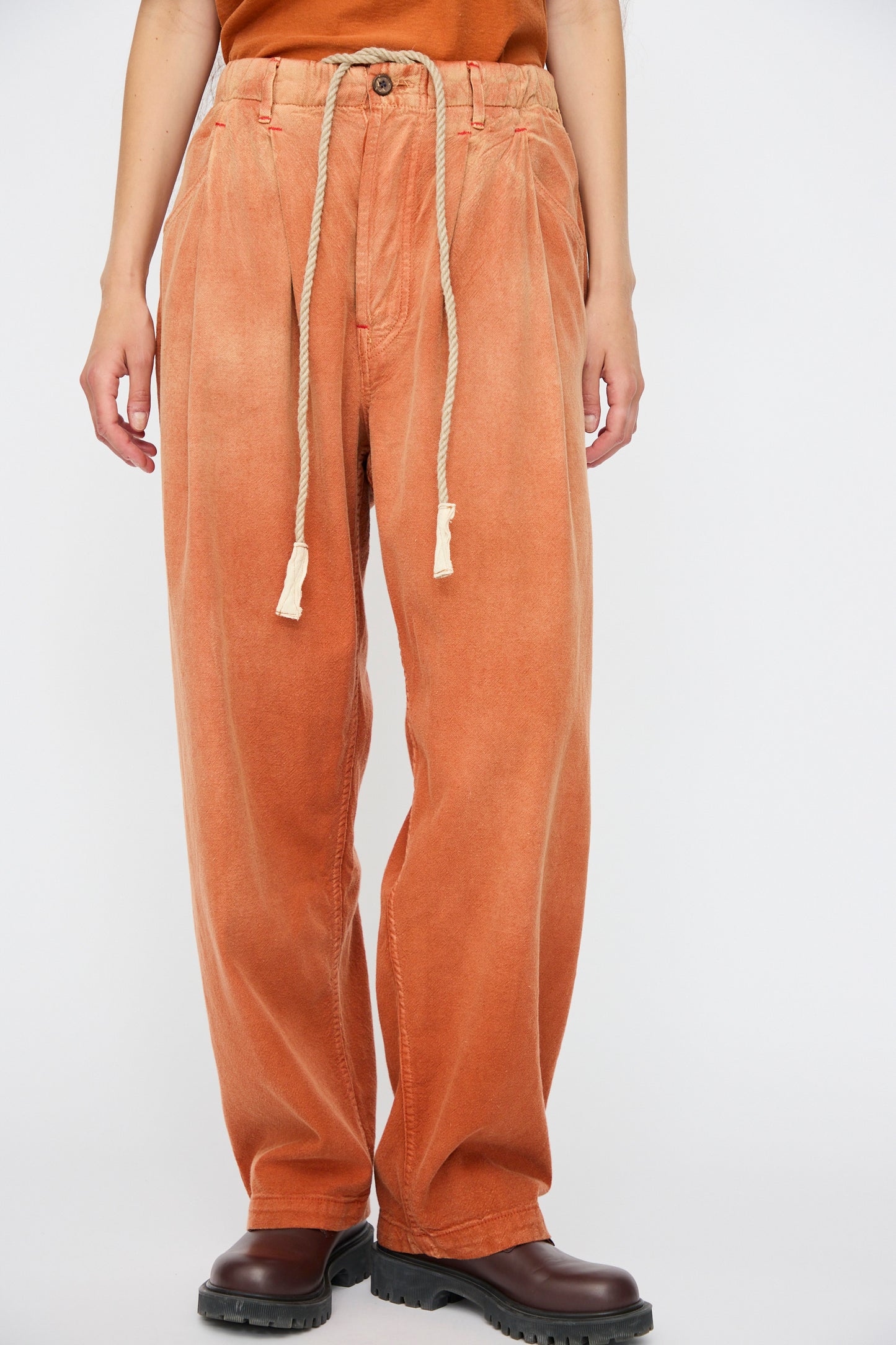 Person wearing Dr. Collectors P40 Z Boys Sunfaded Dye pants in Rust, relaxed fit with elastic waistband, brown boots, and an orange Japanese cotton top; image cropped at the shoulders.