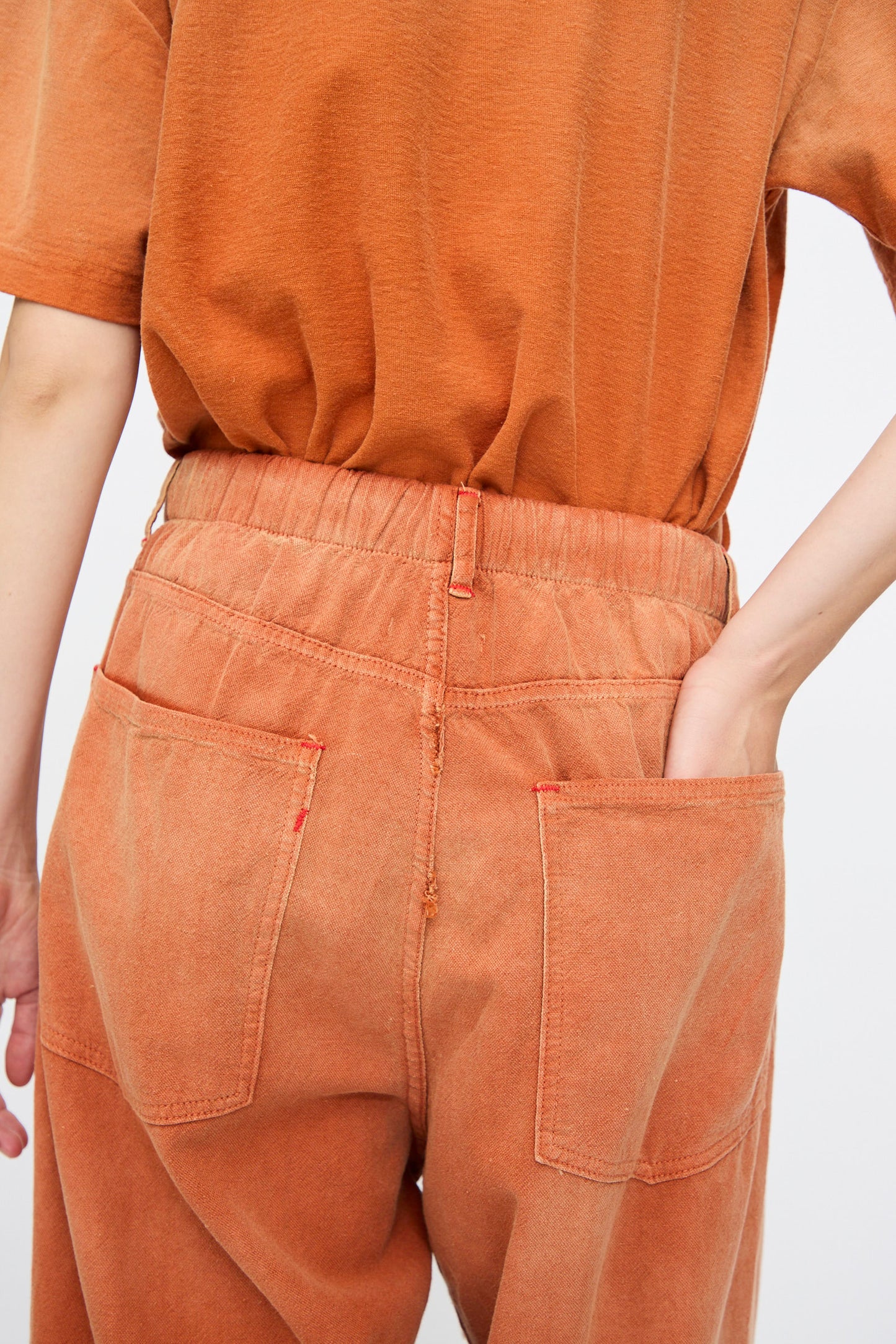 A person is seen from behind wearing Dr. Collectors P40 Z Boys Sunfaded Dye in Rust—relaxed fit pants with an elastic waistband, made from Japanese cotton—with hands in back pockets.
