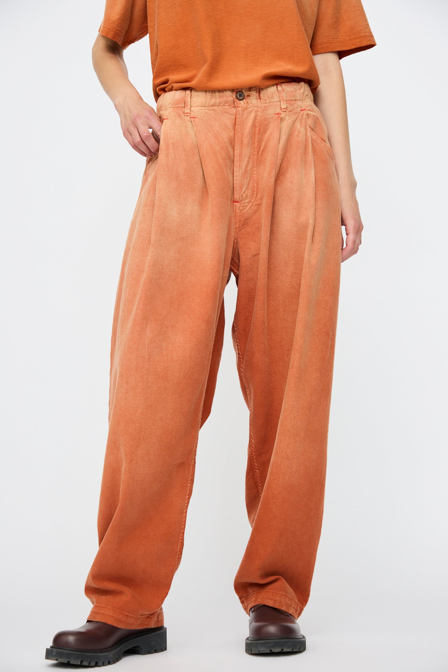 A person wearing Dr. Collectors' P40 Z Boys Sunfaded Dye pants in Rust, paired with an orange t-shirt and dark brown shoes, stands against a plain white background.