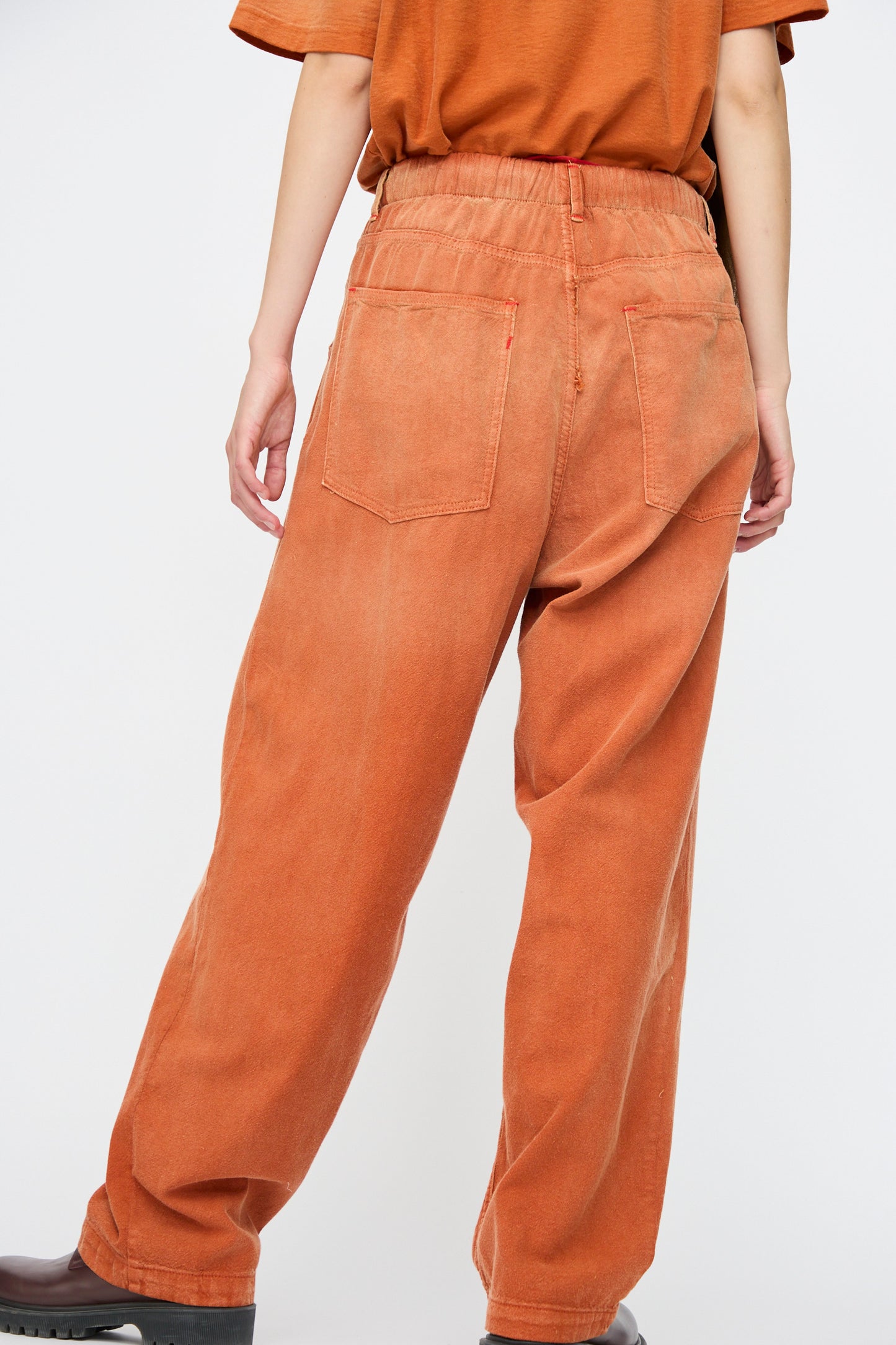 Wearing Dr. Collectors' P40 Z Boys Sunfaded Dye pants in Rust, featuring relaxed fit Japanese cotton, elastic waistband, and back pockets, paired with a matching tee and black shoes against a plain background.