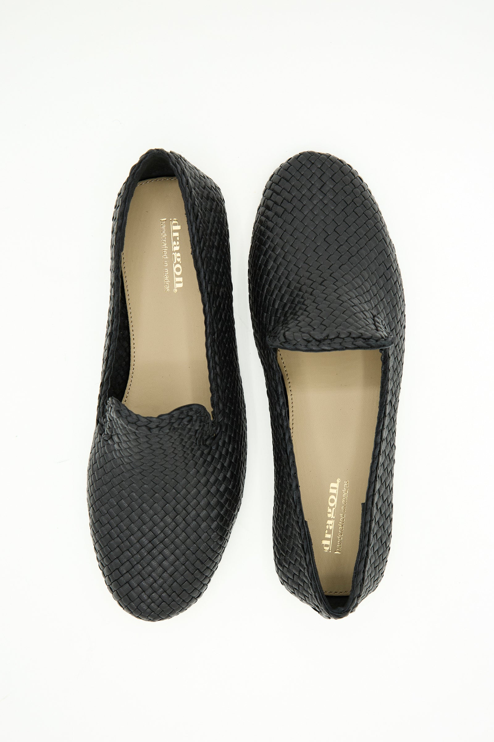 The Damas Slipper in Black by Dragon Diffusion is a pair of black handwoven leather slippers with tan insoles, shown from above on a white background.