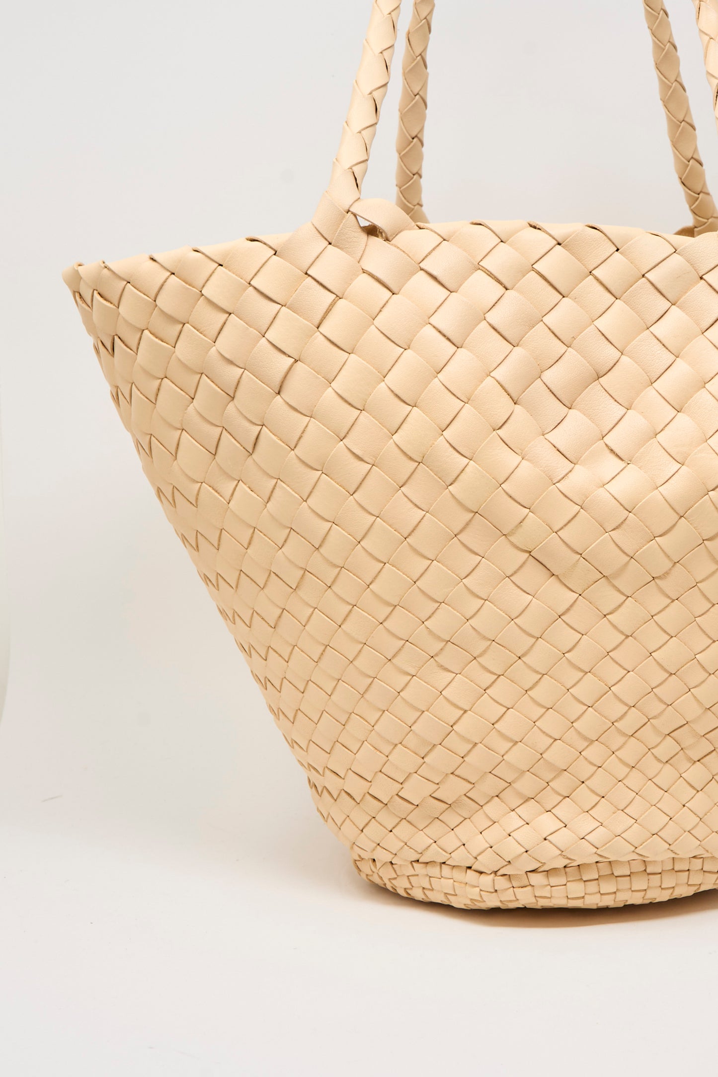 Close-up of the Egola in Natural, a beige woven leather handbag with two handles by Dragon Diffusion, handmade in India and displayed against a plain light background.