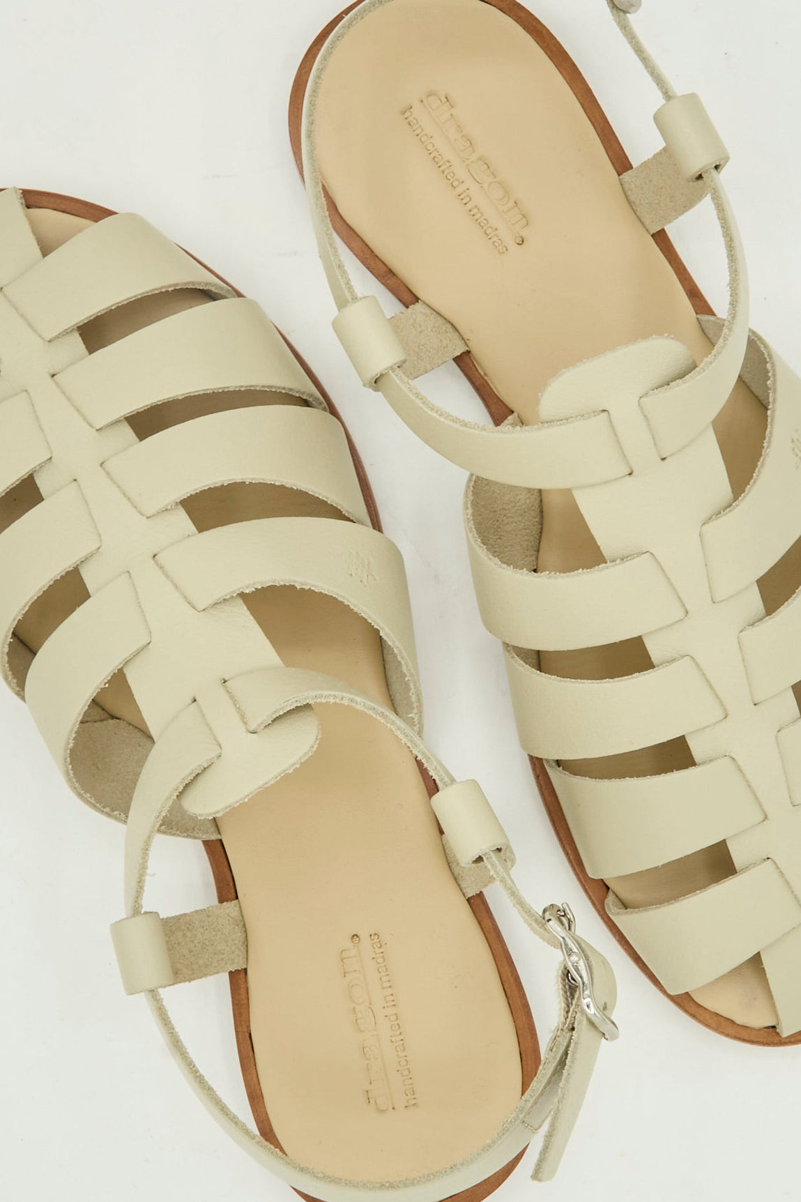 The Dragon Diffusion Pescador Sandal in Pearl features handcrafted beige woven cow leather, ankle straps, and flat brown soles, shown on a white background.