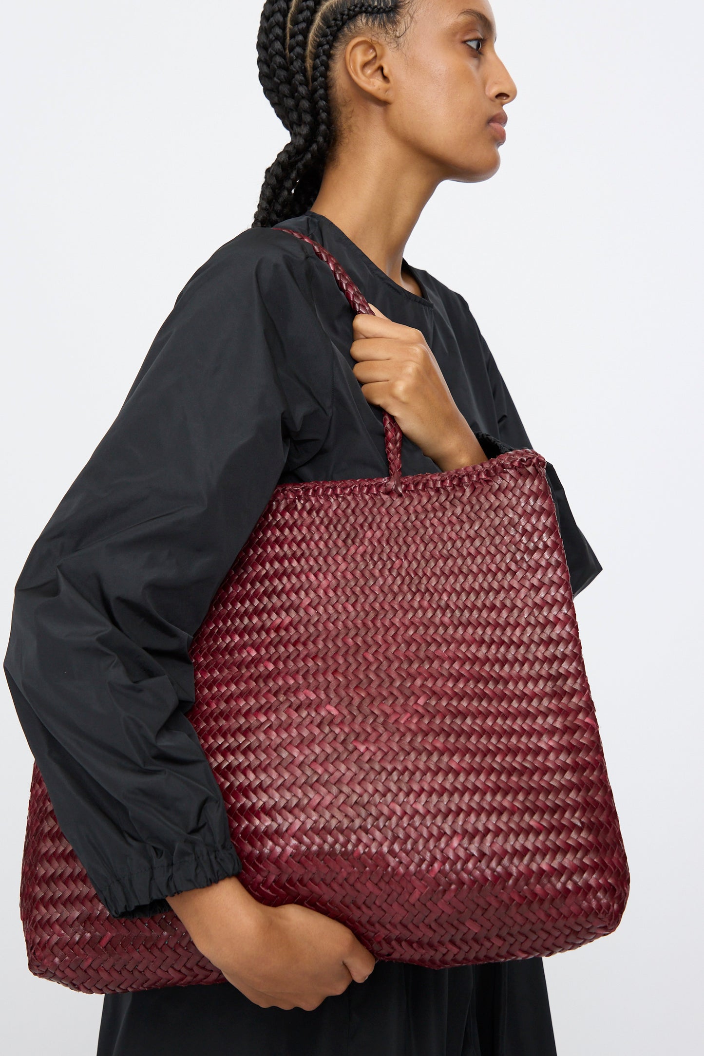 Person in a black top holds the Dragon Diffusion Sophie Large in Bordo, a handwoven leather bag, against a plain background.