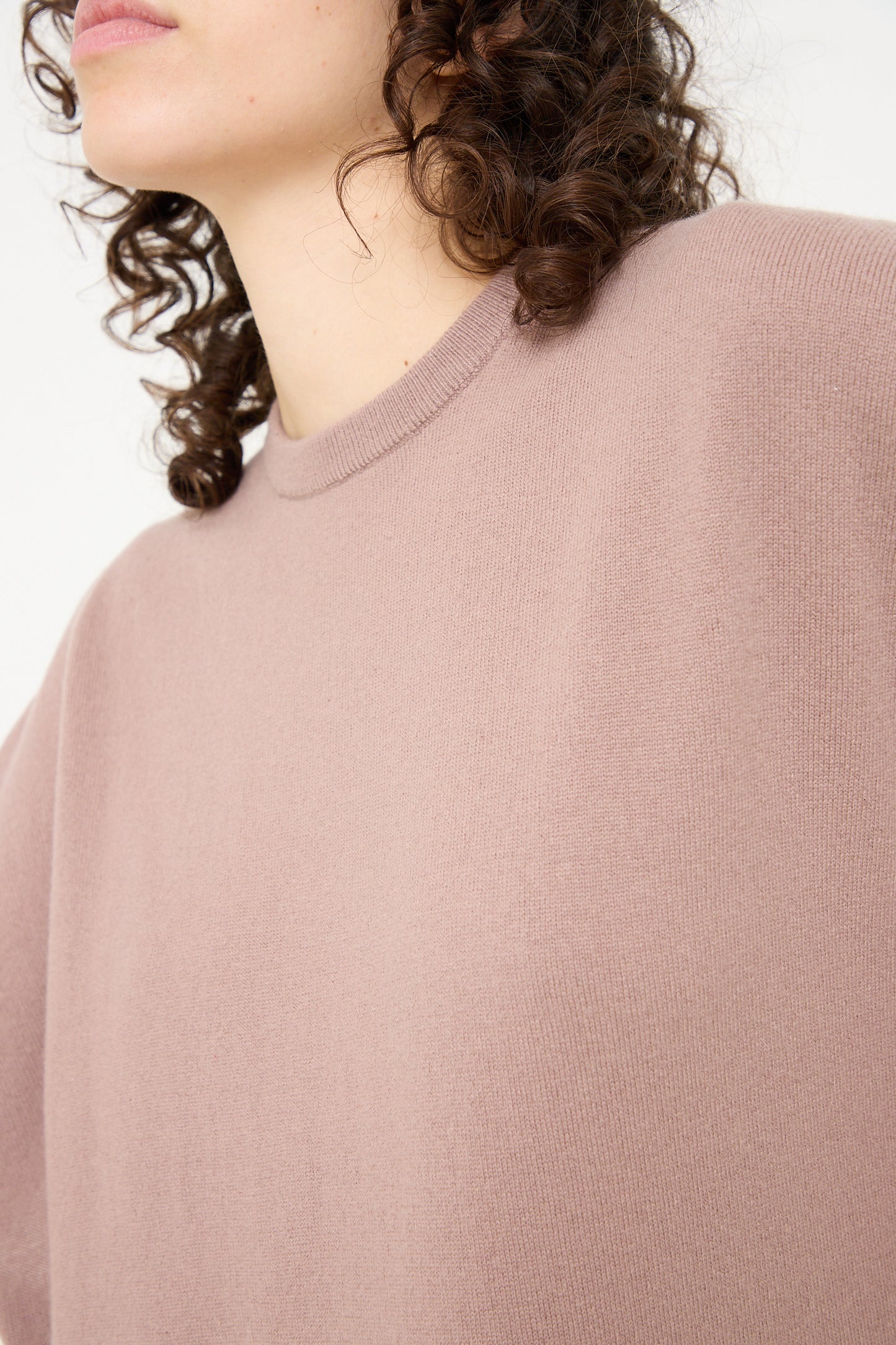 The model is wearing a pink Extreme Cashmere cashmere sweater with curly hair.