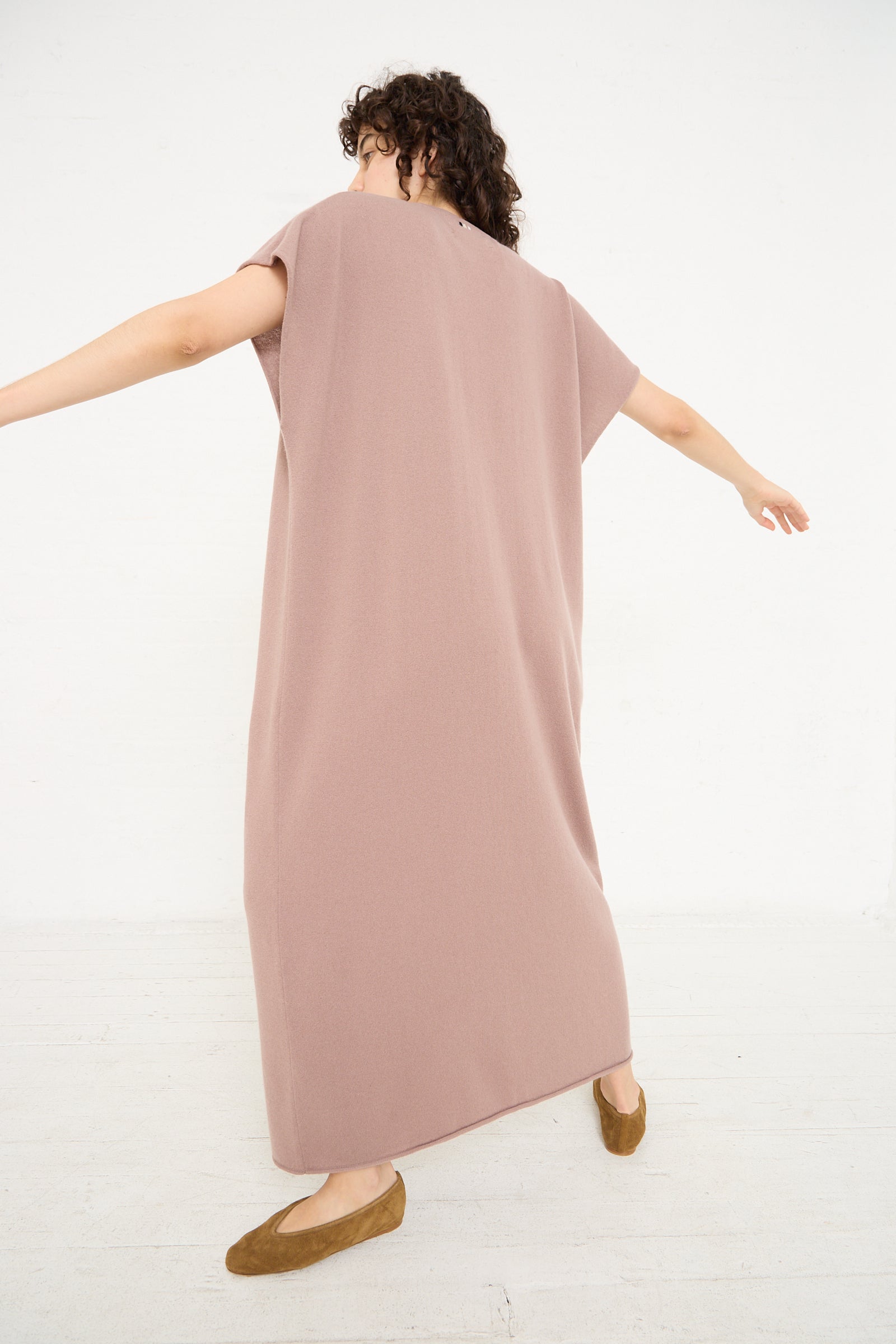 A woman in a pink No. 169 Healing Dress in Clay by Extreme Cashmere with her arms outstretched.
