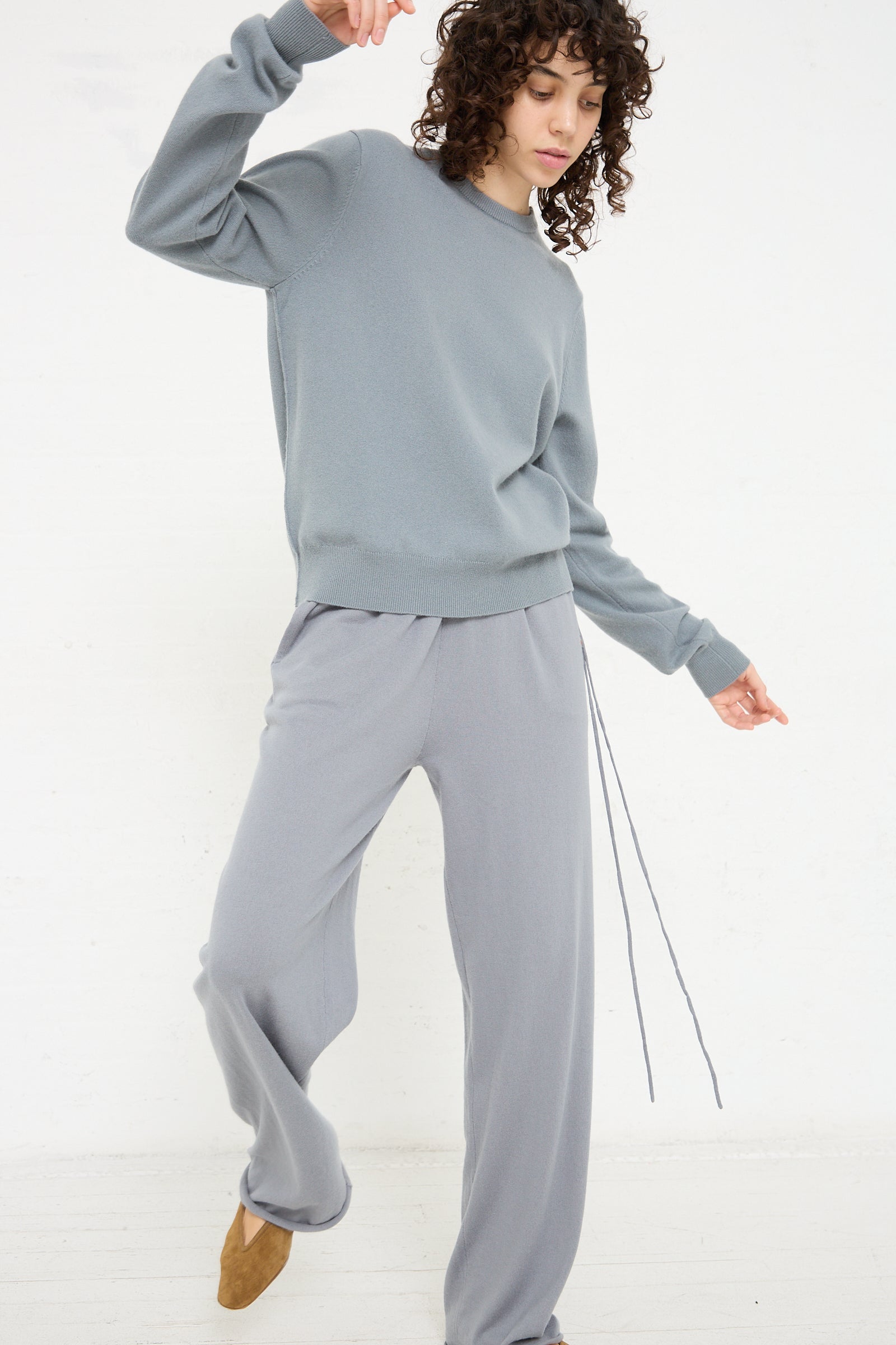 The model is wearing Extreme Cashmere's No. 278 Judo Pant in Sage and a grey sweatshirt for a comfortable look.