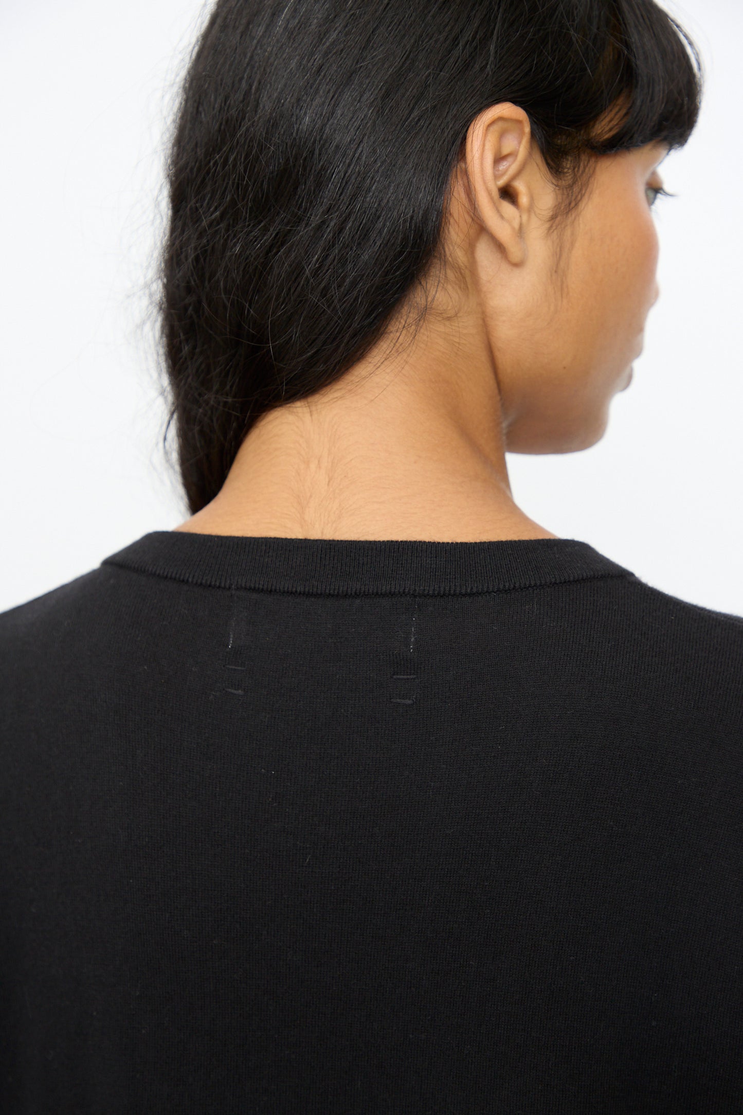 A person with long dark hair, seen from behind, wears the Extreme Cashmere No. 410 Inda Dress in Raven—a black maxi t-shirt dress featuring faint neckline stitching and a relaxed silhouette.