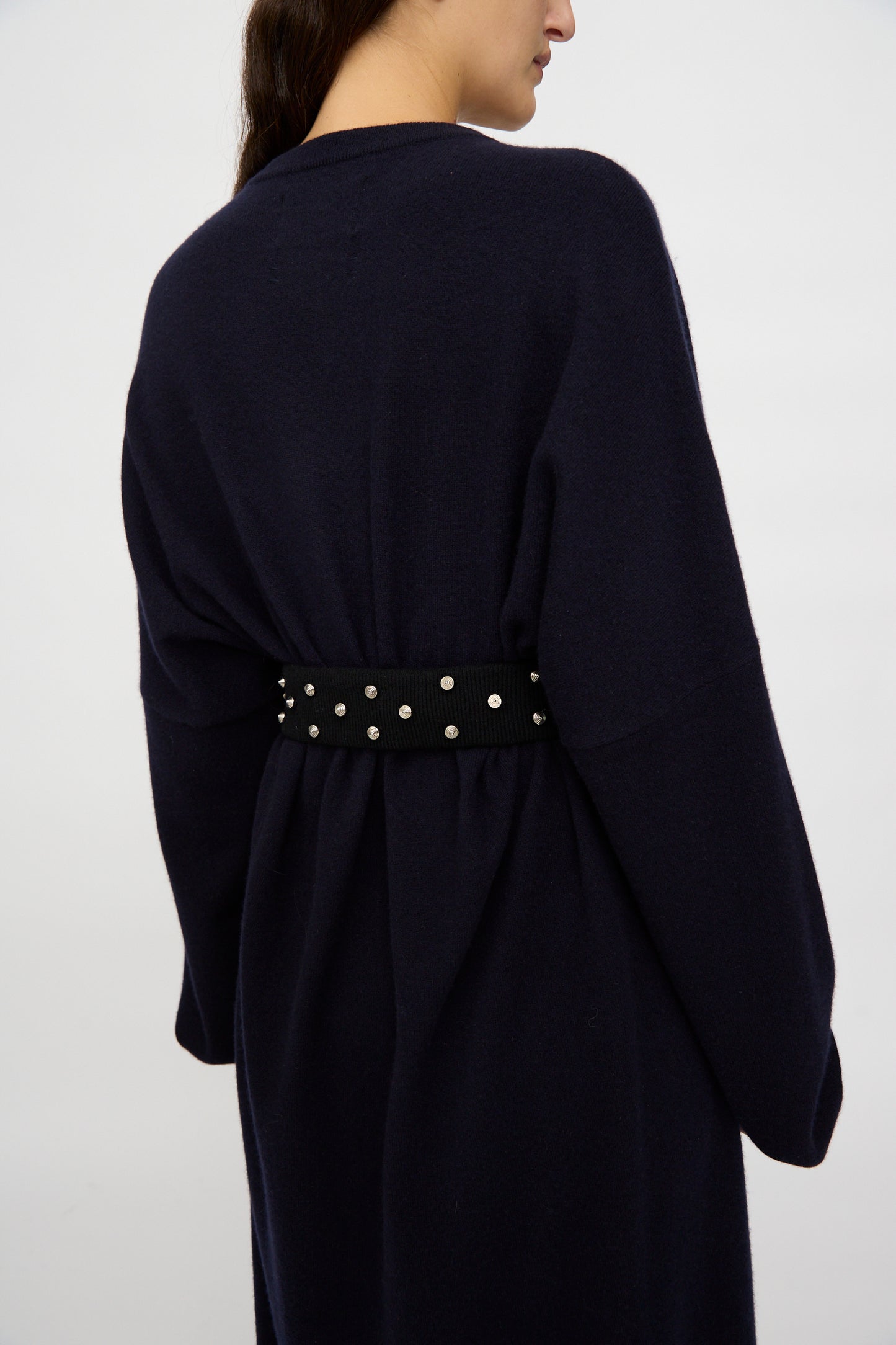 Photographed from behind against a plain background, a person wears a dark navy, long-sleeved coat styled with the Extreme Cashmere No. 446 Stud Belt at the waist.