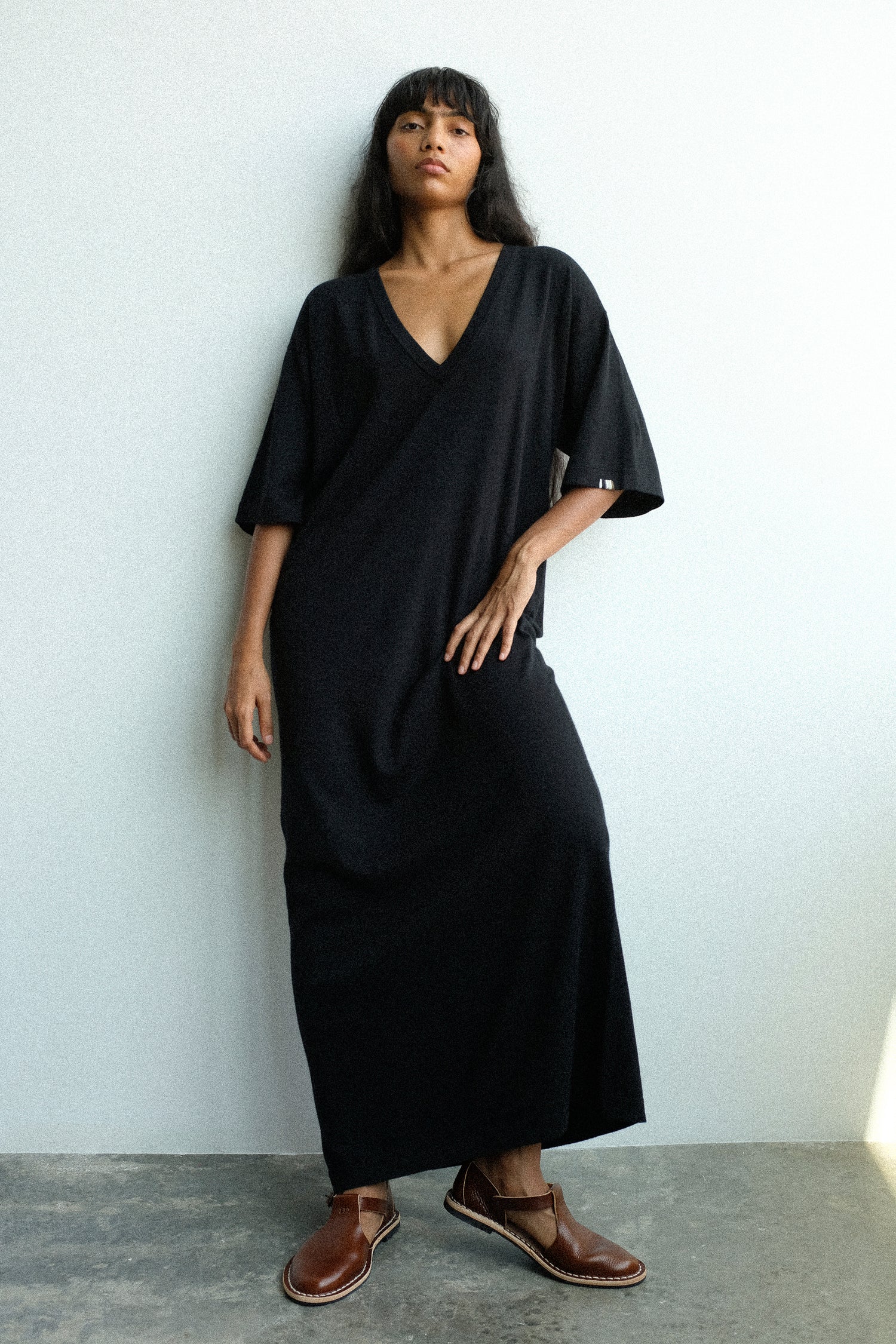 Woman wearing a black dress by Extreme Cashmere standing against a white wall.