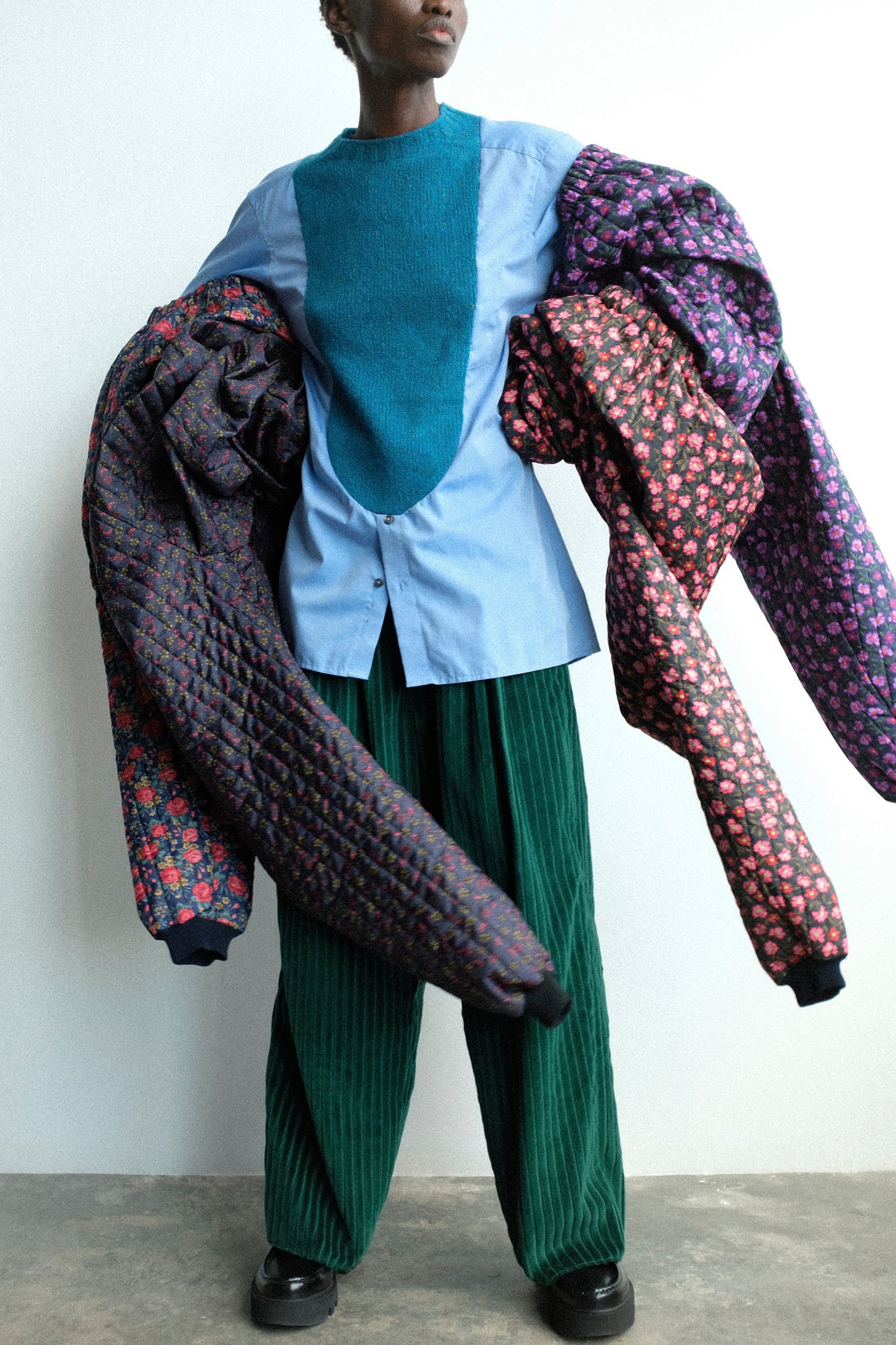 A woman holding four pairs of pants on her arms against a white background.
