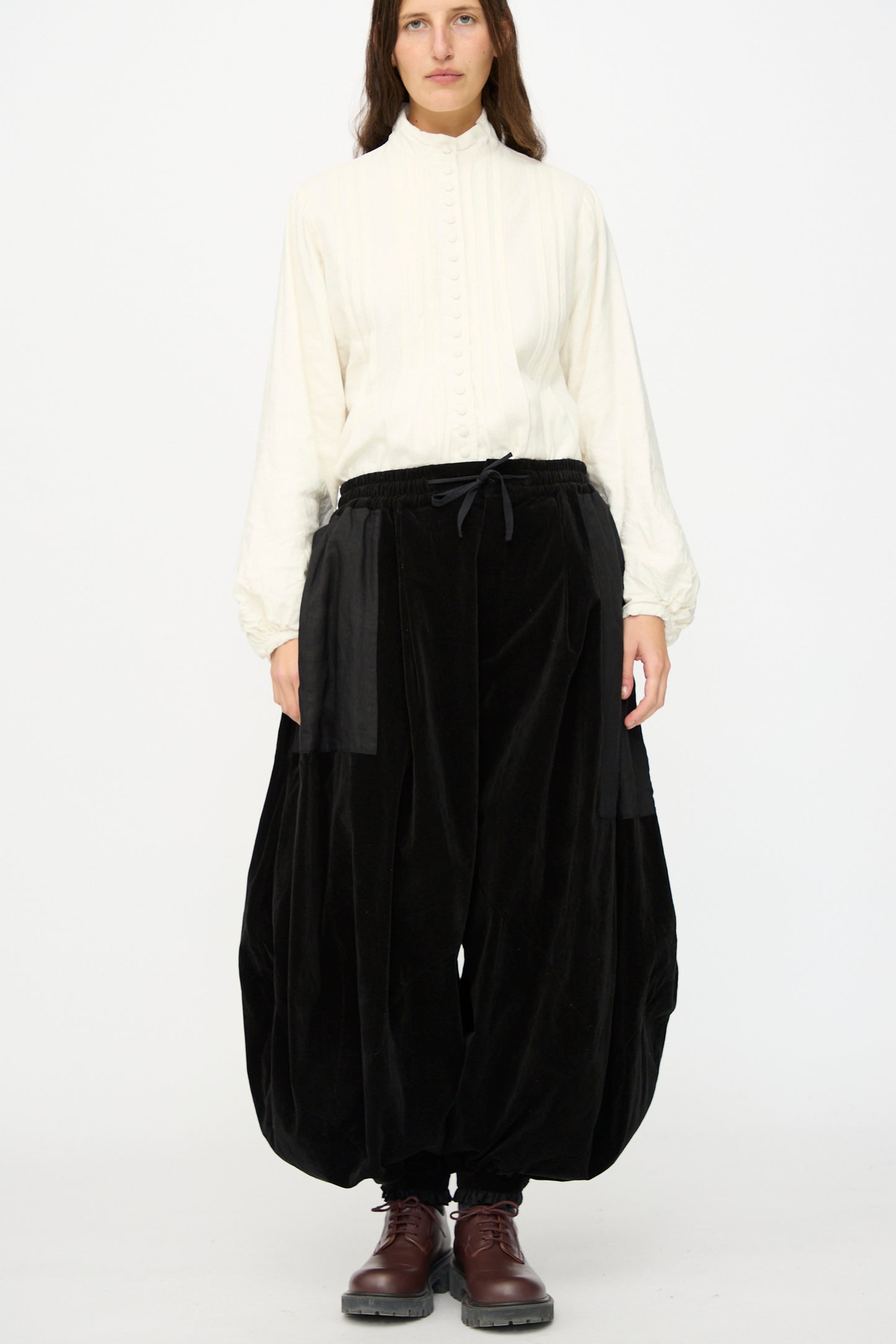 A person stands against a plain background wearing Hallelujah's Bloomer in Black, paired with a high-neck white blouse and brown lace-up boots.