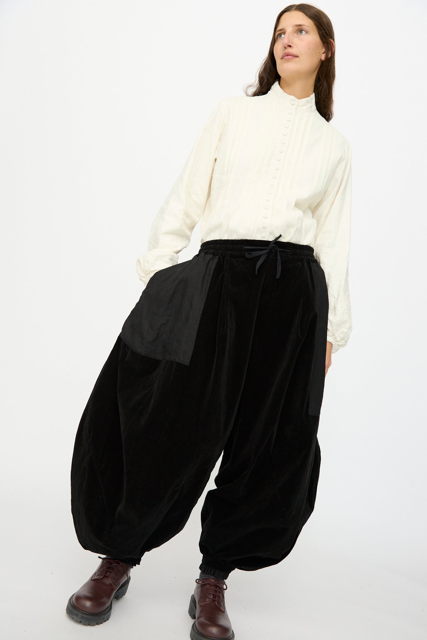 A person stands against a plain white background wearing Hallelujah's Bloomer in Black, paired with a white button-up shirt and brown boots.