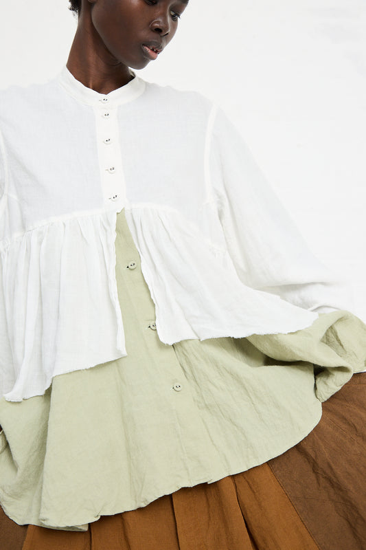 A person donning a layered outfit featuring a Hallelujah Chemise in Sage, handmade in Kyoto, over a light green shirt and a brown skirt.