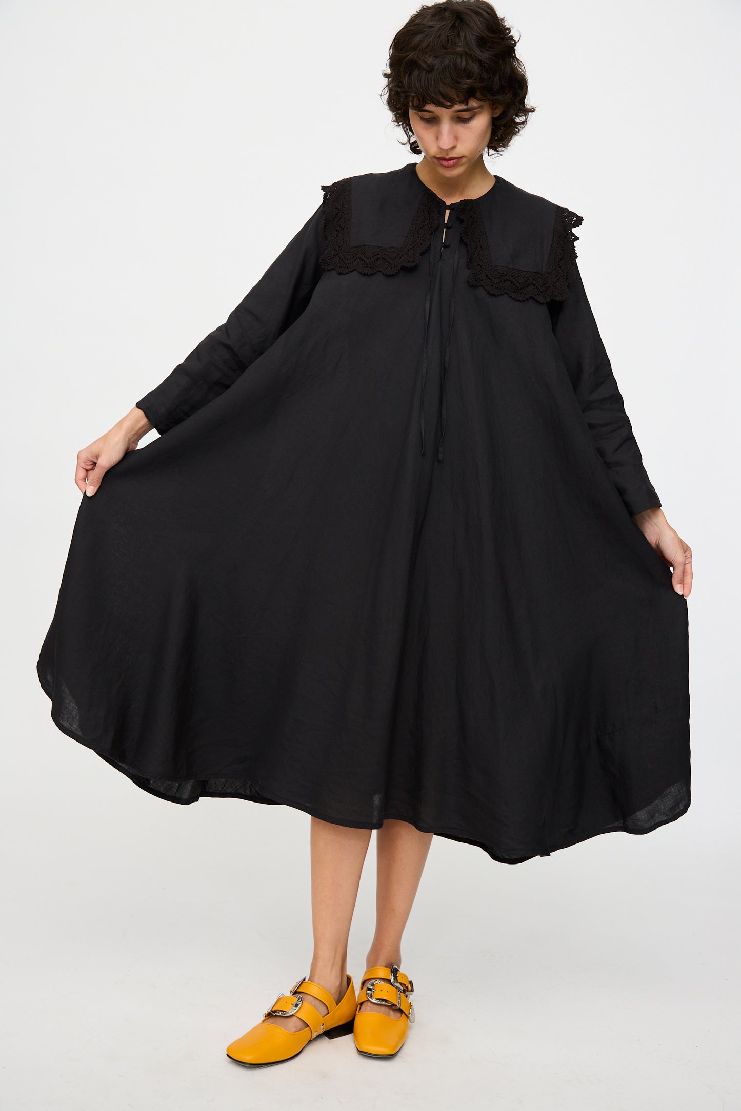A model showcases the width of the Robe Religieuse col carré in Black by Hallelujah, wearing eye-catching yellow shoes against a plain white background.