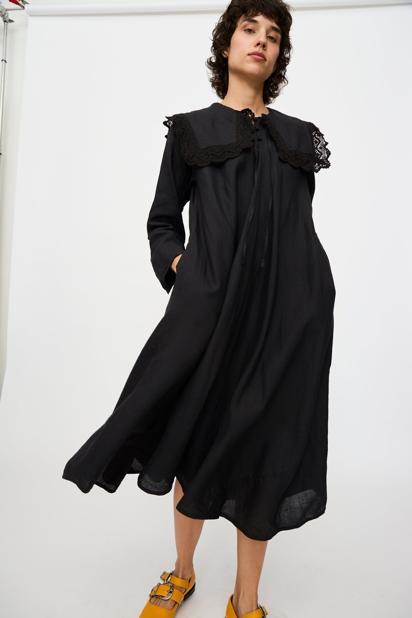 A person wearing Hallelujah's Robe Religieuse col carré in black pairs it with yellow shoes against a plain backdrop.