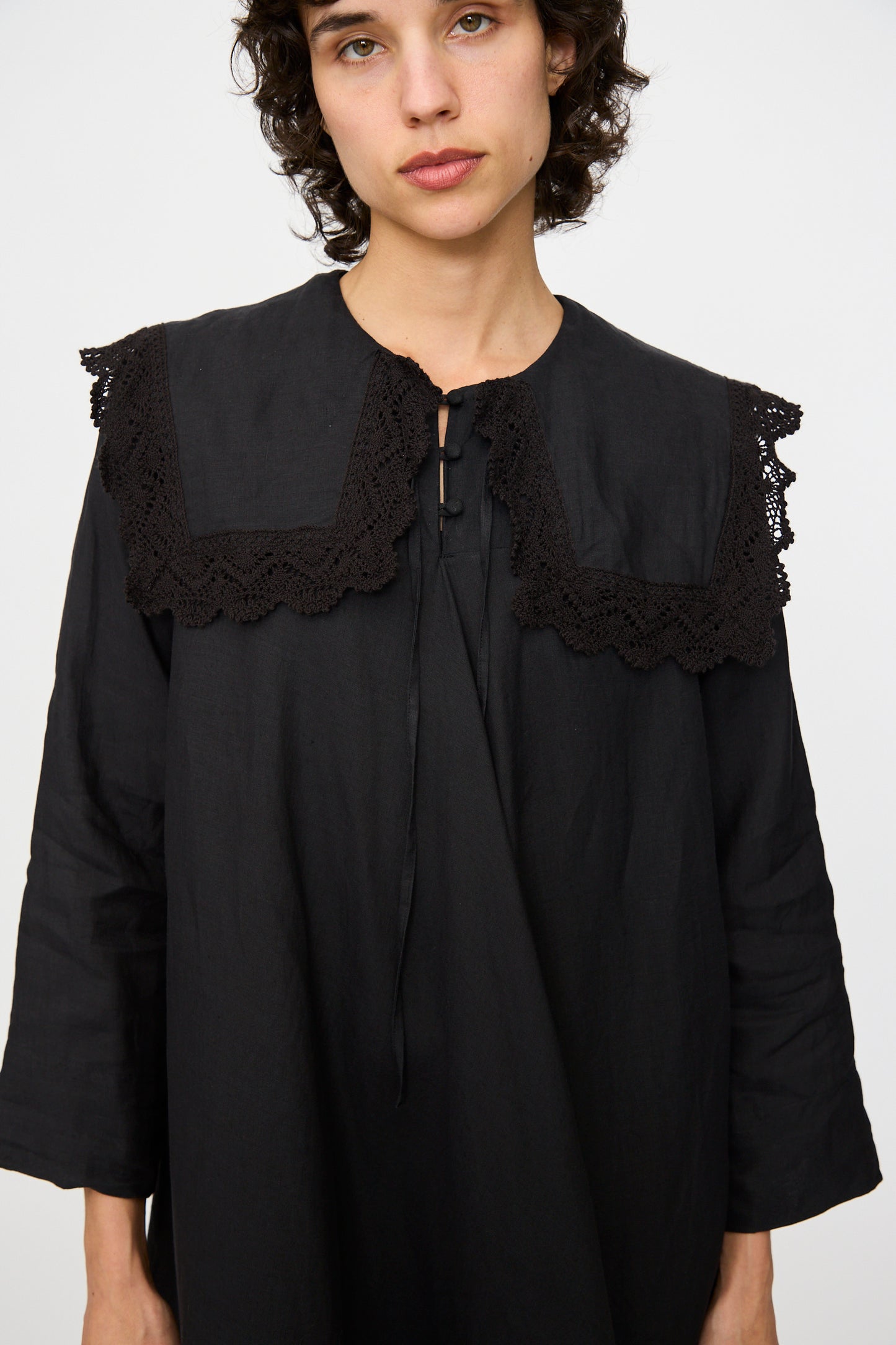 A person wearing the Hallelujah Robe Religieuse col carré in black, featuring a crochet lace collar, while looking at the camera against a plain background.