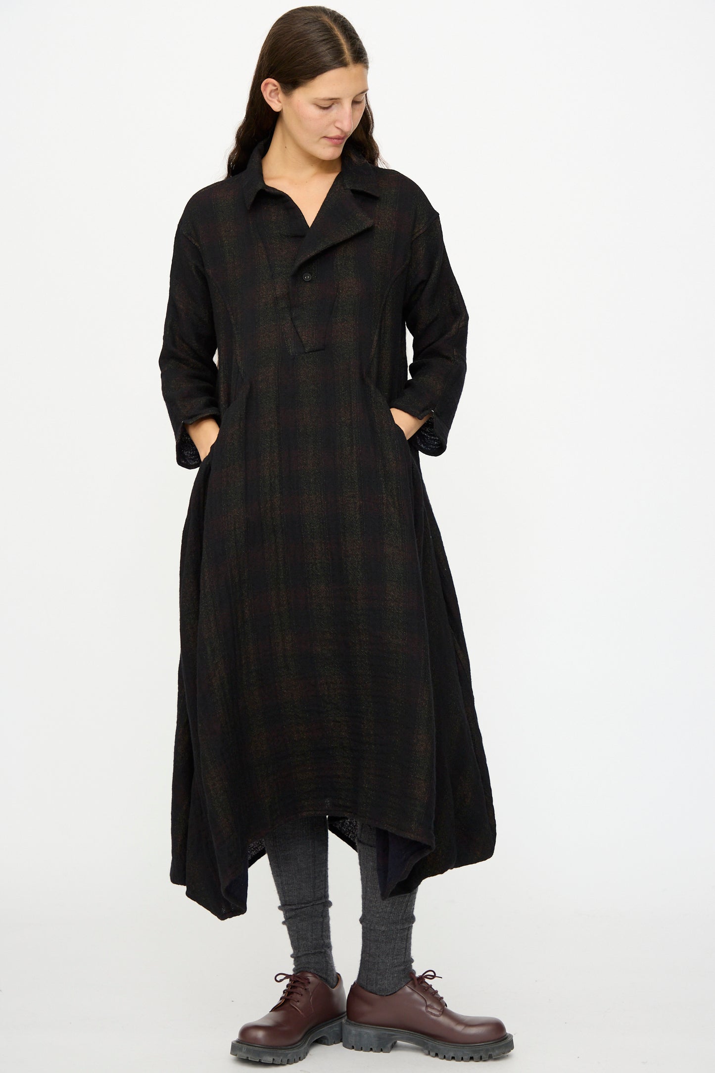A woman stands with hands in pockets, wearing the Hallelujah Wool Cotton Robe de Berger in Black Mix, gray leggings, and brown lace-up shoes against a plain white background.