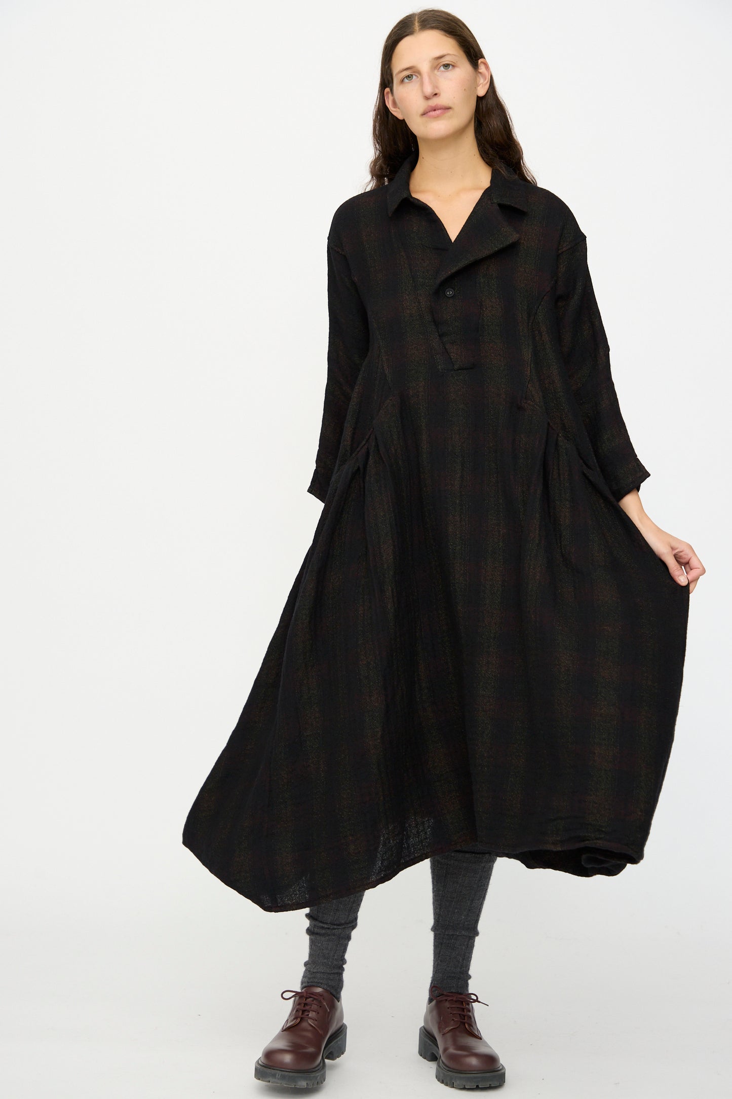 A woman wears the Hallelujah Wool Cotton Robe de Berger in Black Mix, styled with gray leggings and brown lace-up shoes, standing against a plain white background.