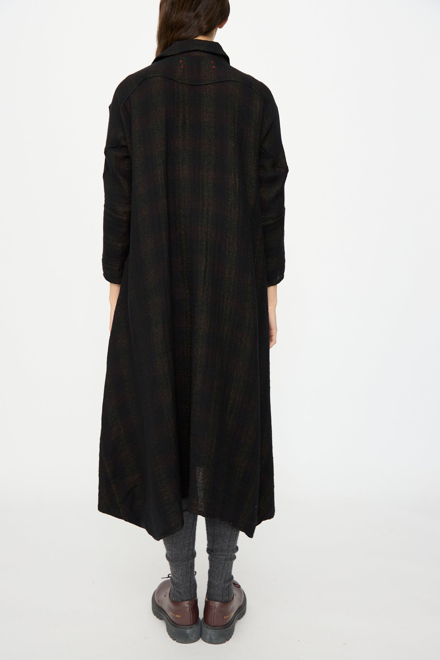 A person stands with their back to the camera against a plain white background, wearing Hallelujah's Wool Cotton Robe de Berger in Black Mix, paired with gray leggings and brown shoes. Made in Japan.