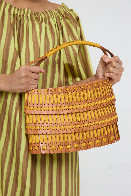 Woman holding a Hatori Basket Bag 168 in Tan and Yellow against a green striped dress.
