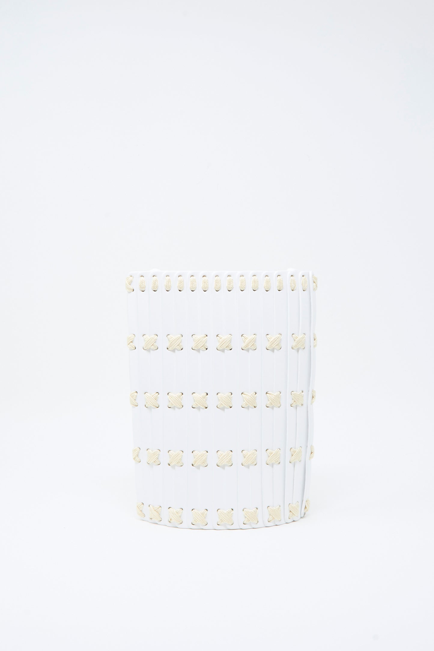 A white cylindrical Leather Crossbody 30 by Hatori, featuring vertical ridges and a grid of small, beige floral motifs reminiscent of the delicate patterns found on handcrafted vegetable-tanned leather goods, accented with white lacing.