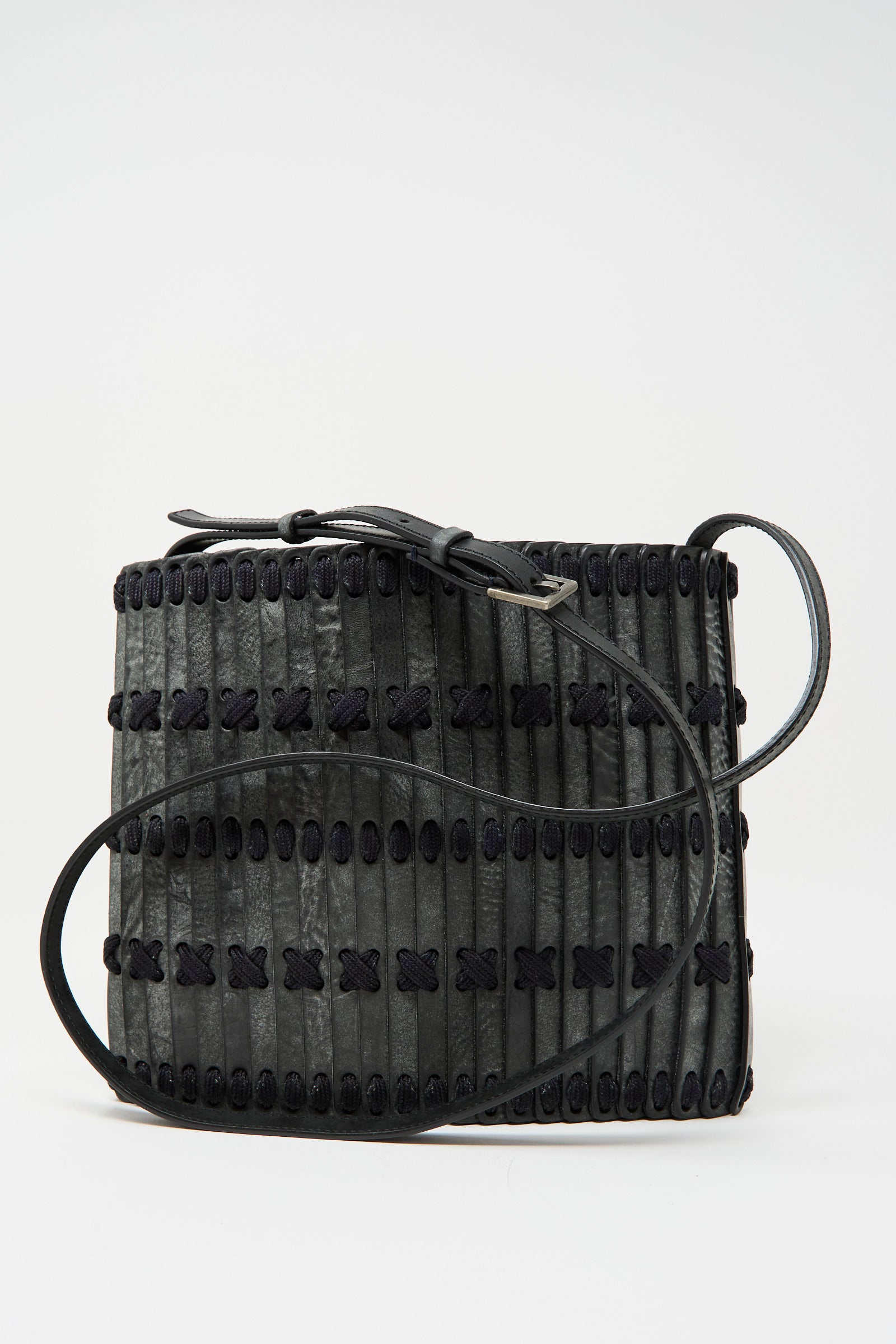 The Hatori Leather Crossbody 48 Bag in waxed coated black with indigo lace features a handcrafted rectangular design, decorative stitching, vertical strips, and an adjustable shoulder strap, shown against a plain background.