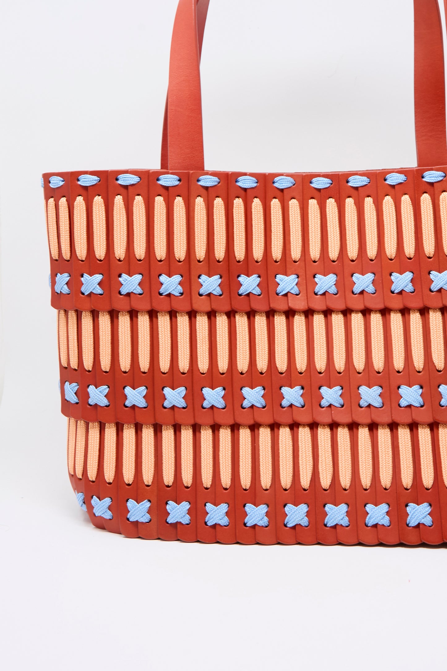 The Hatori Leather Tote 198 Artist Edition with Alex Dodge in Red is a large tote bag, expertly crafted from vegetable tanned leather, featuring a red base, yellow vertical slits, blue X-shaped stitches, layered horizontal panels, and a red strap—all set against a white background.