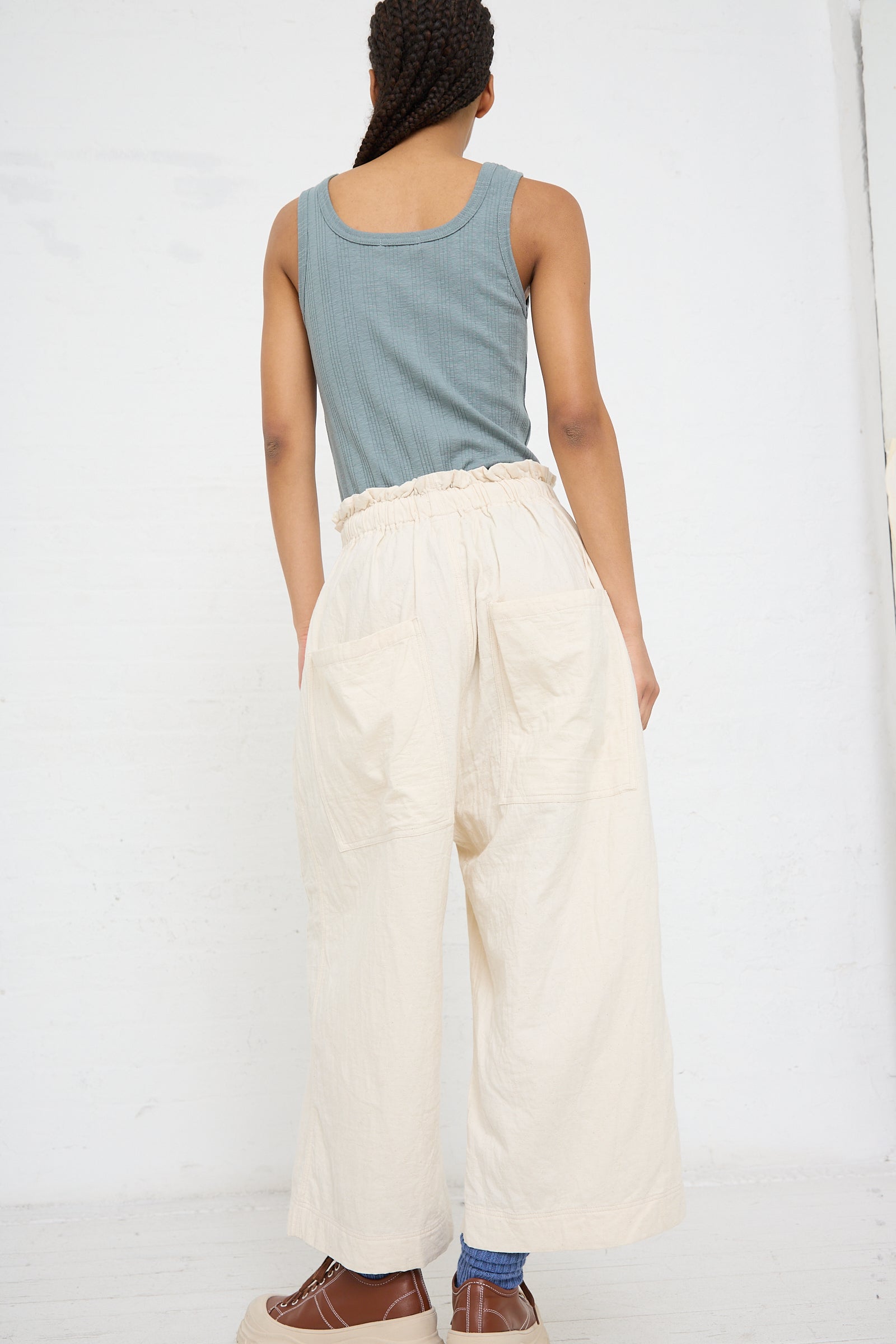 A person seen from behind wearing Azumadaki Cotton Quilt Pant in Ivory by Ichi Antiquités, a blue tank top, and brown shoes.