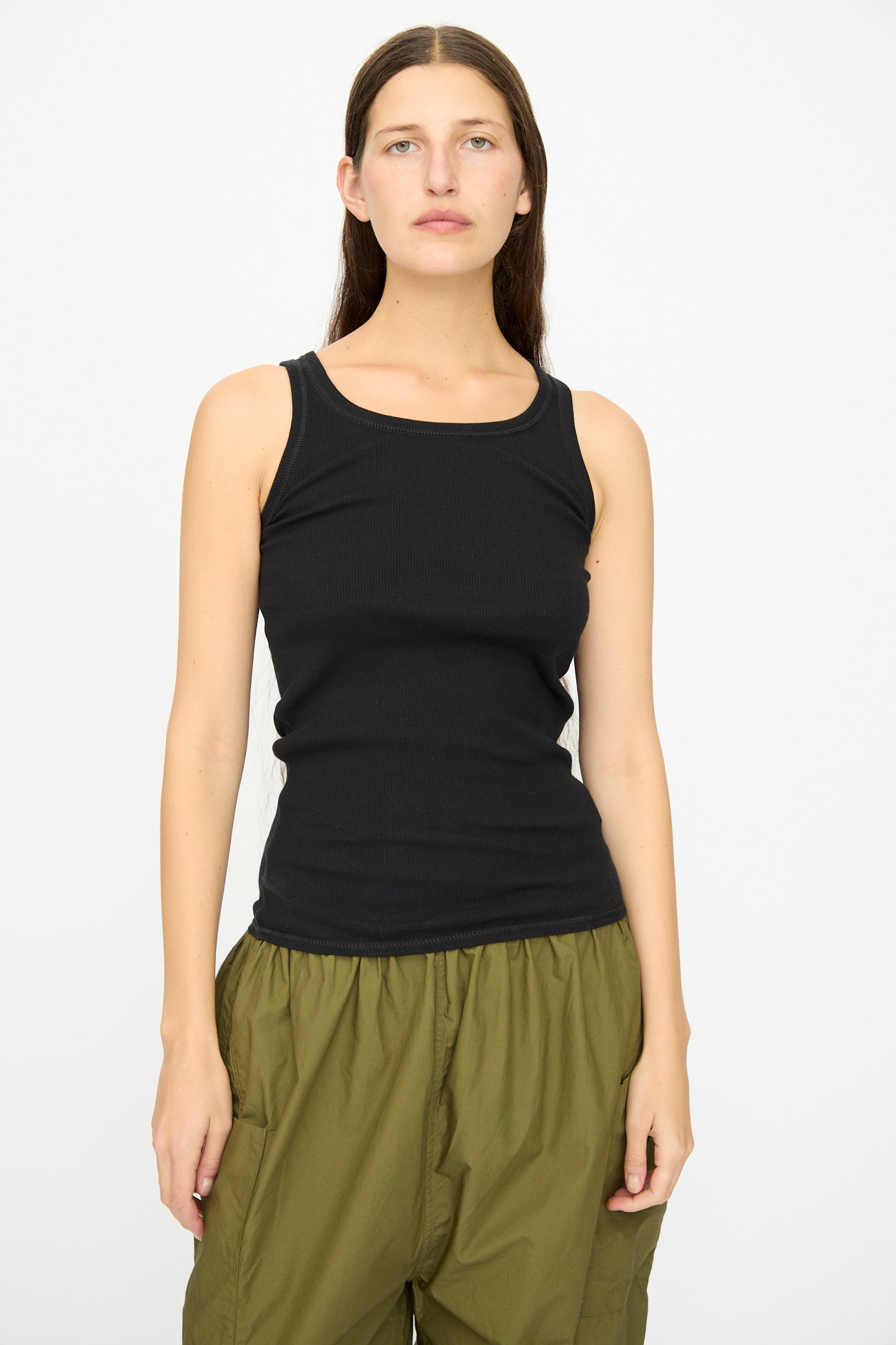 A person with long brown hair wears the Ichi Antiquités Cotton Cashmere Tank Top in Black, paired with olive green pants, standing against a plain white background.