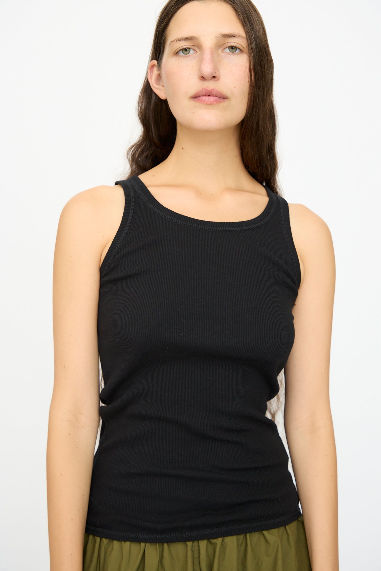 A woman with long brown hair wears the Ichi Antiquités Cotton Cashmere Tank Top in Black, paired with olive green pants, standing against a plain white background.