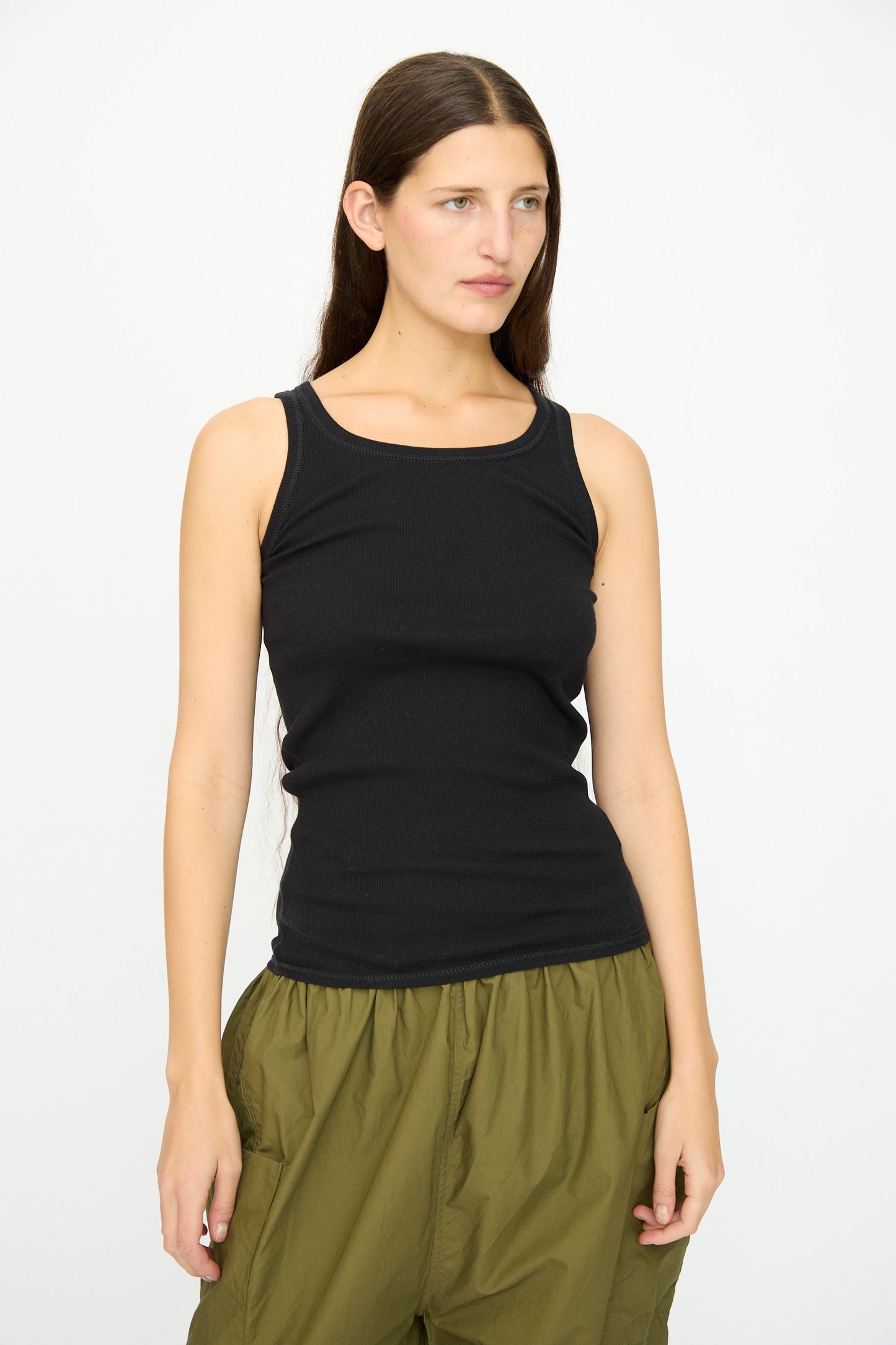 A woman with long brown hair wears the Ichi Antiquités Cotton Cashmere Tank Top in Black and olive green pants, standing against a plain white background.