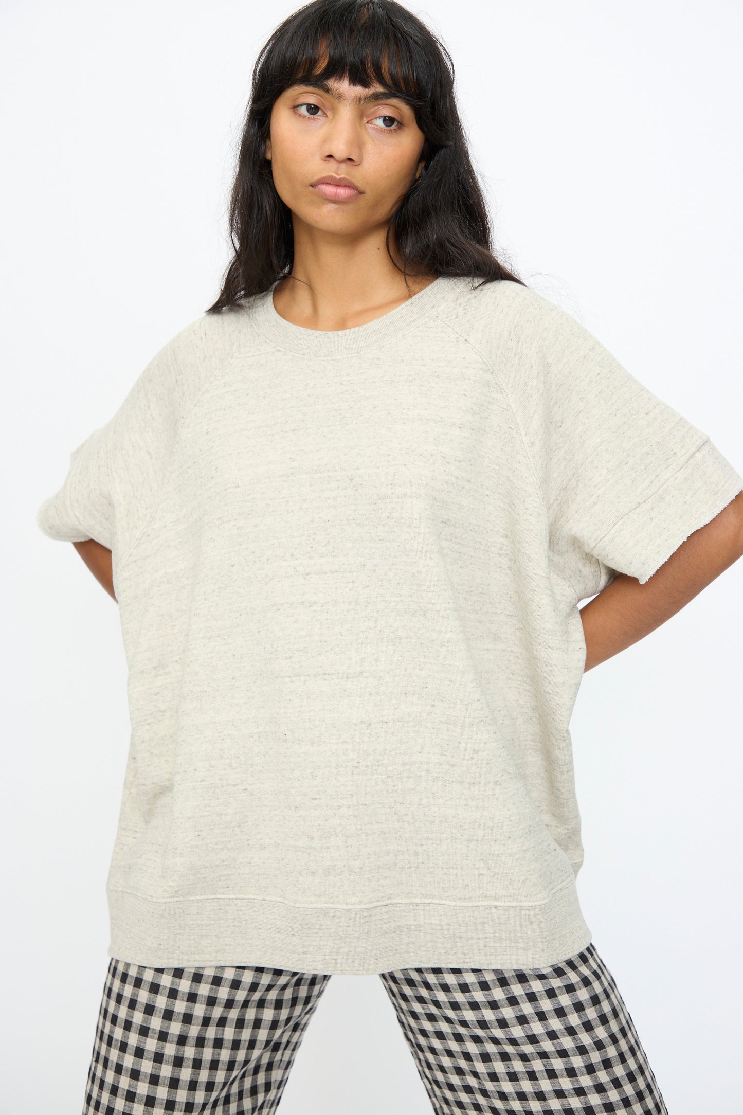 A woman stands against a plain background wearing the Cotton Fleece Pullover in Gray by Ichi Antiquités and black-and-white checkered pants, both made in Japan.