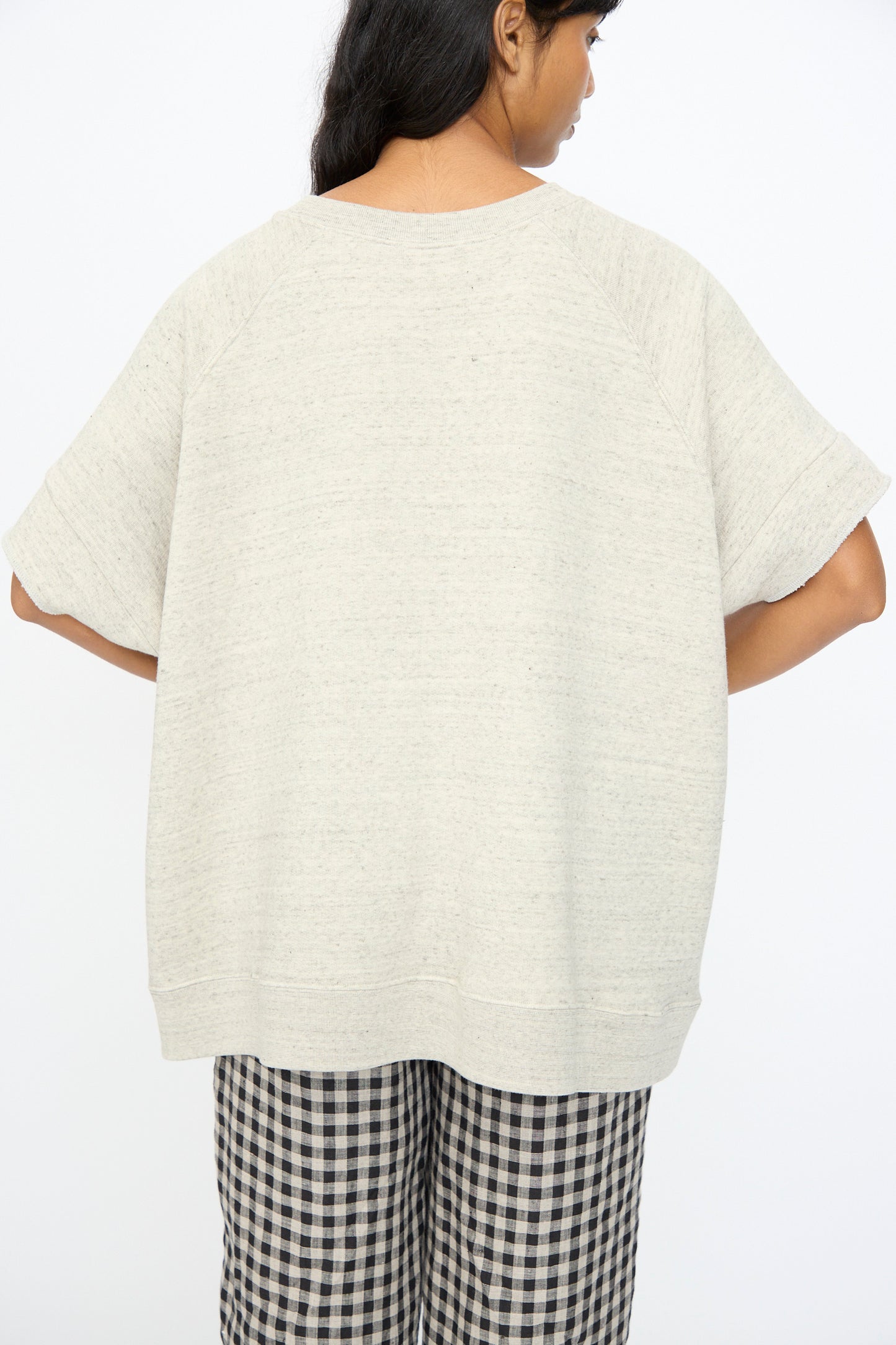 A person with long dark hair, seen from behind, wears the Ichi Antiquités Cotton Fleece Pullover in Gray and black-and-white checkered pants.