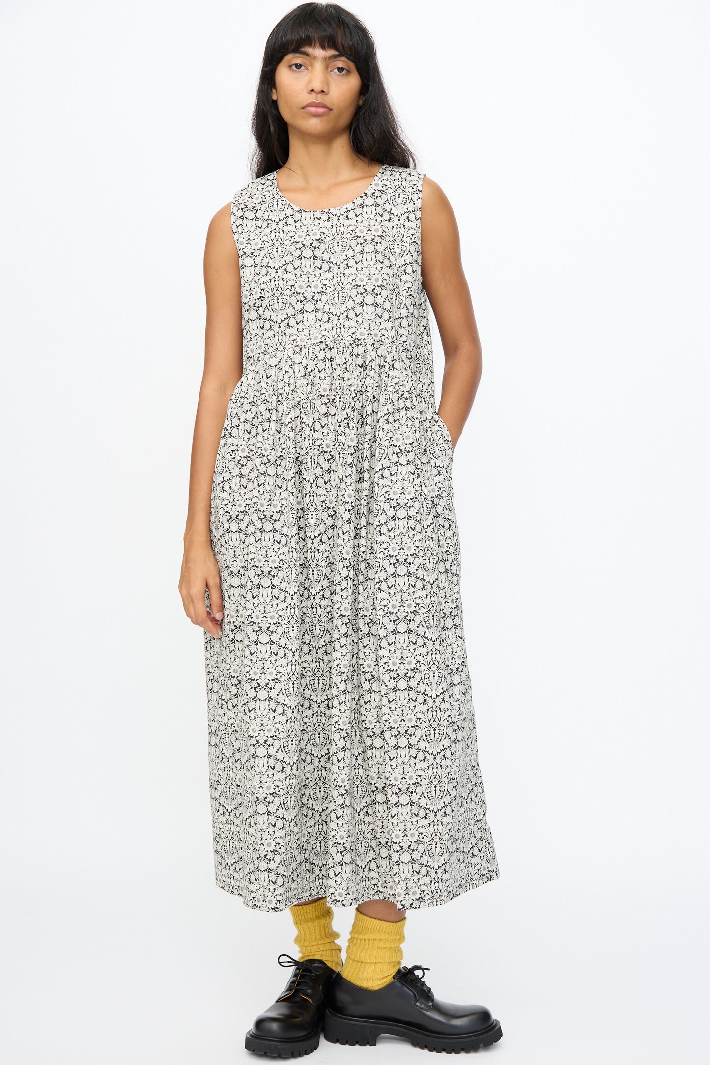 A person wears the Ichi Antiquités Cotton Liberty Dress in Natural and Black, paired with yellow socks and black lace-up shoes, standing against a plain white background.