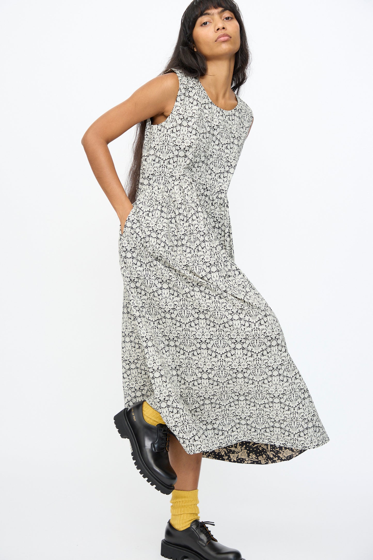 A person wears the Ichi Antiquités Cotton Liberty Dress in Natural and Black, paired with yellow socks and black shoes, standing against a plain white background.