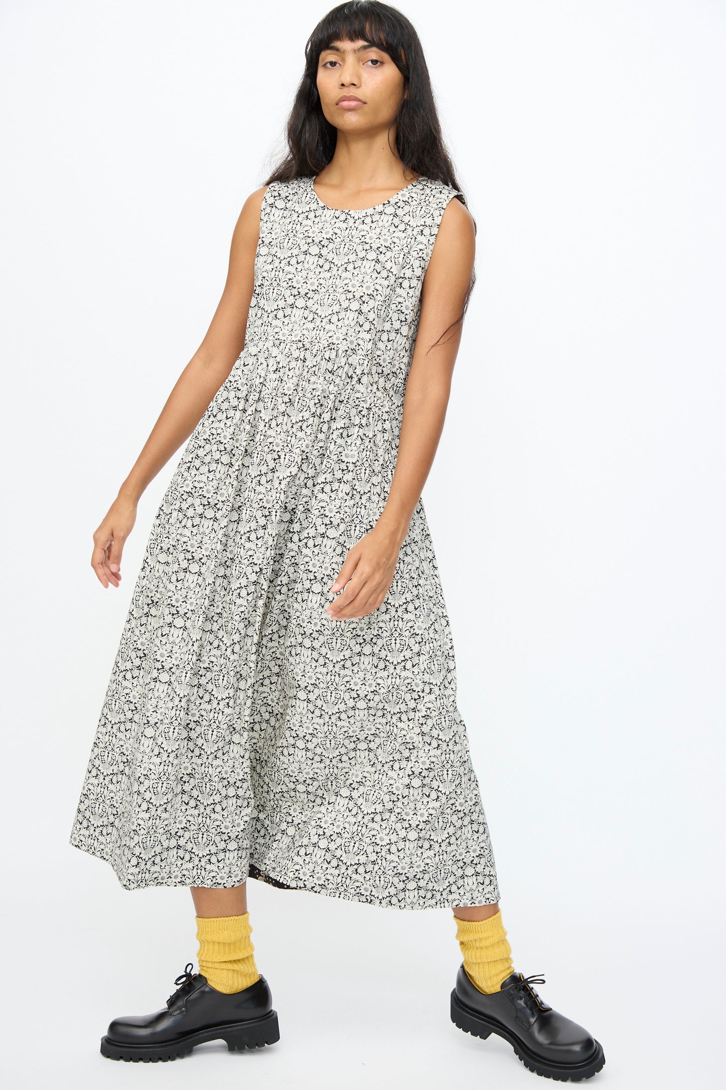 A woman stands against a plain white background wearing the Ichi Antiquités Cotton Liberty Dress in Natural and Black, paired with yellow socks and black shoes.