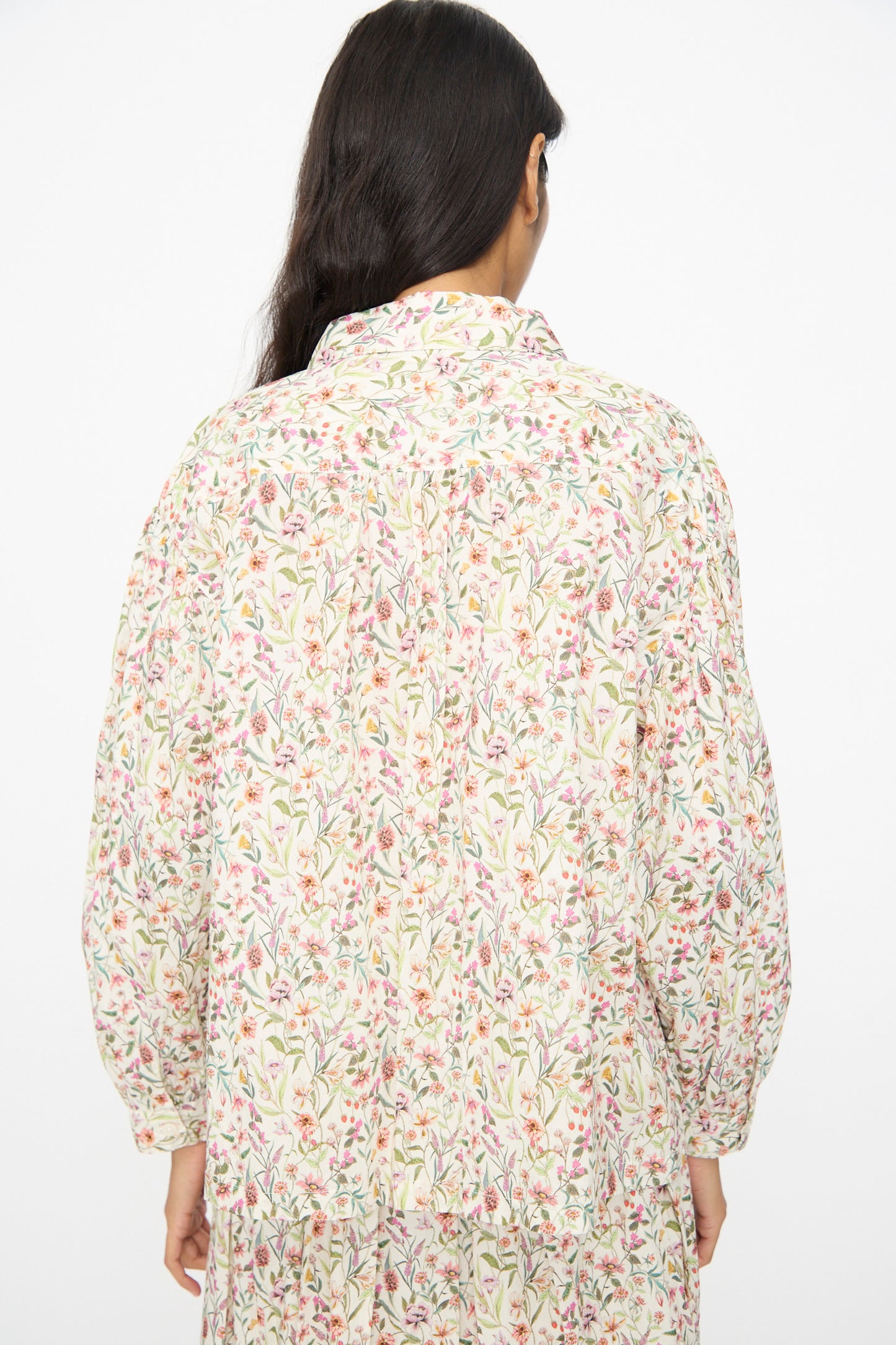 A person with long dark hair is seen from the back wearing the Ichi Antiquités Cotton Liberty Shirt in Flower Print, a light-colored, long-sleeved top.