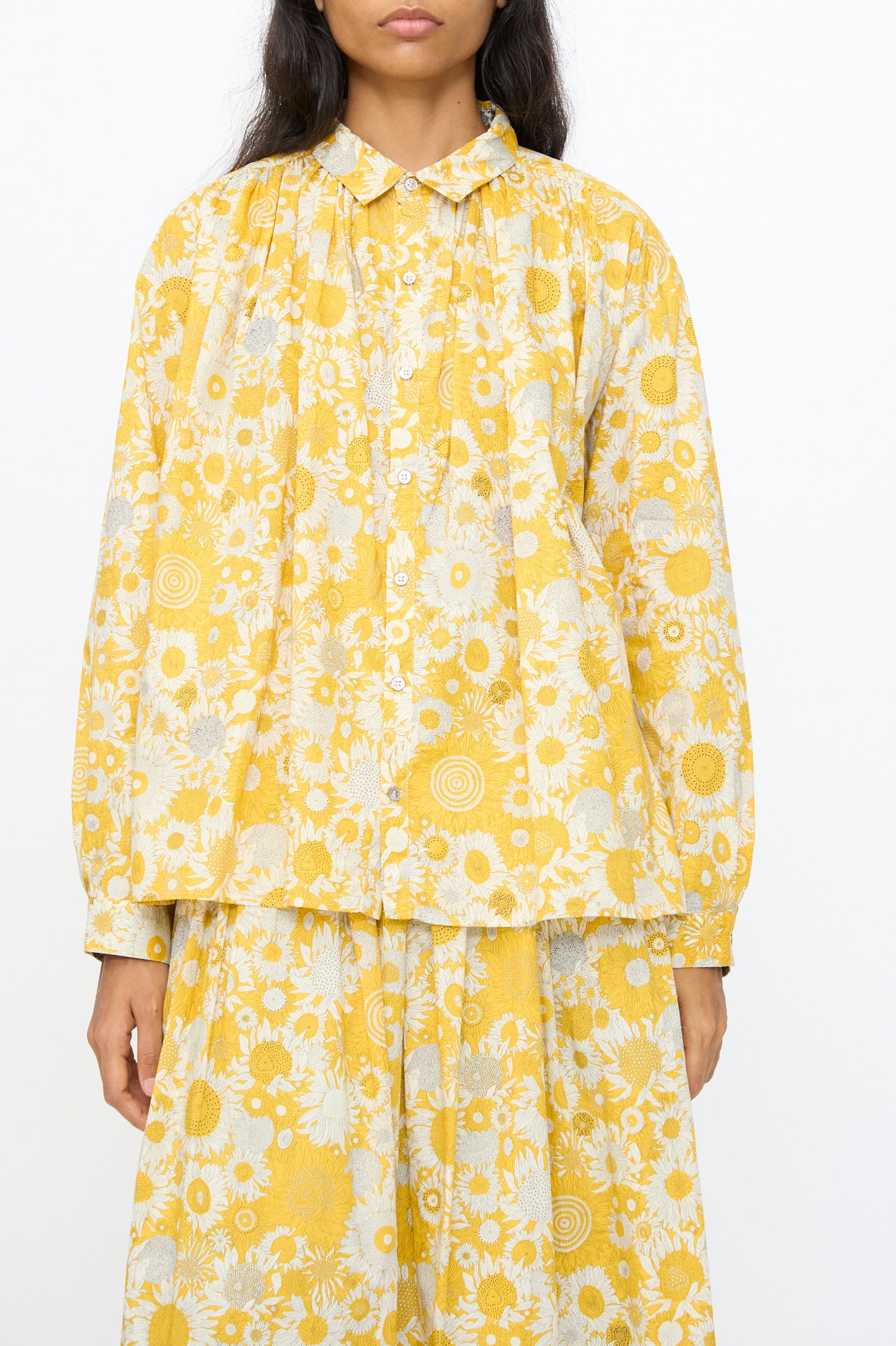 A model wears the Ichi Antiquités Cotton Liberty Shirt in Yellow—a loose-fitting, long-sleeved button-up with a white floral pattern—paired with the matching skirt, standing against a plain white background.