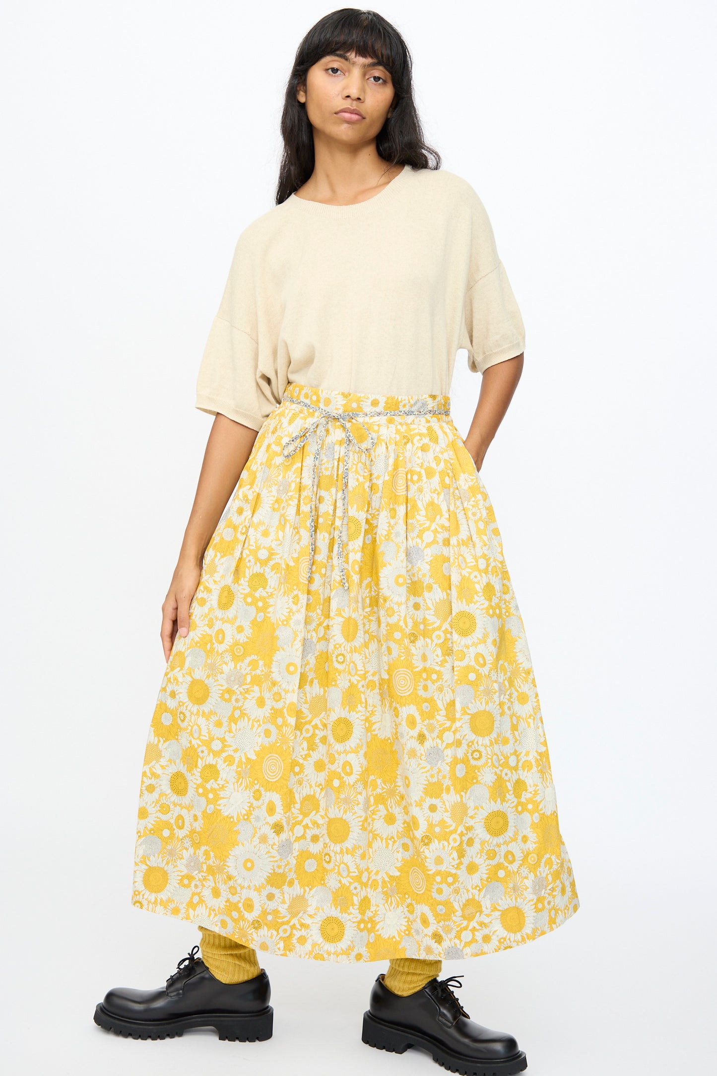 Person wearing a beige short-sleeve top, the Ichi Antiquités Cotton Liberty Skirt in Yellow, yellow socks, and black shoes stands against a plain white background.