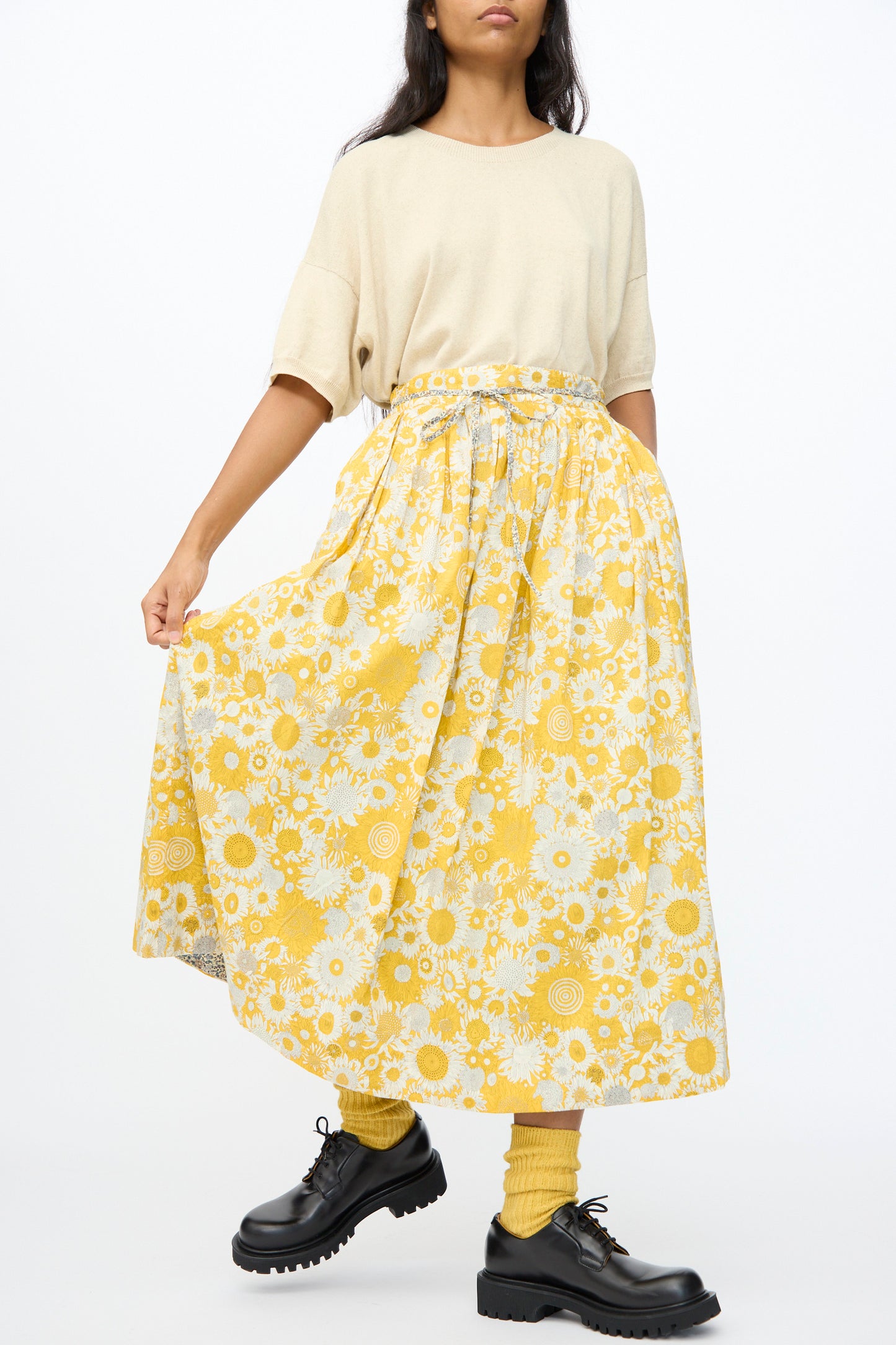 A person stands against a white background wearing a cream short-sleeve top, yellow socks, black chunky shoes, and the Ichi Antiquités Cotton Liberty Skirt in Yellow.