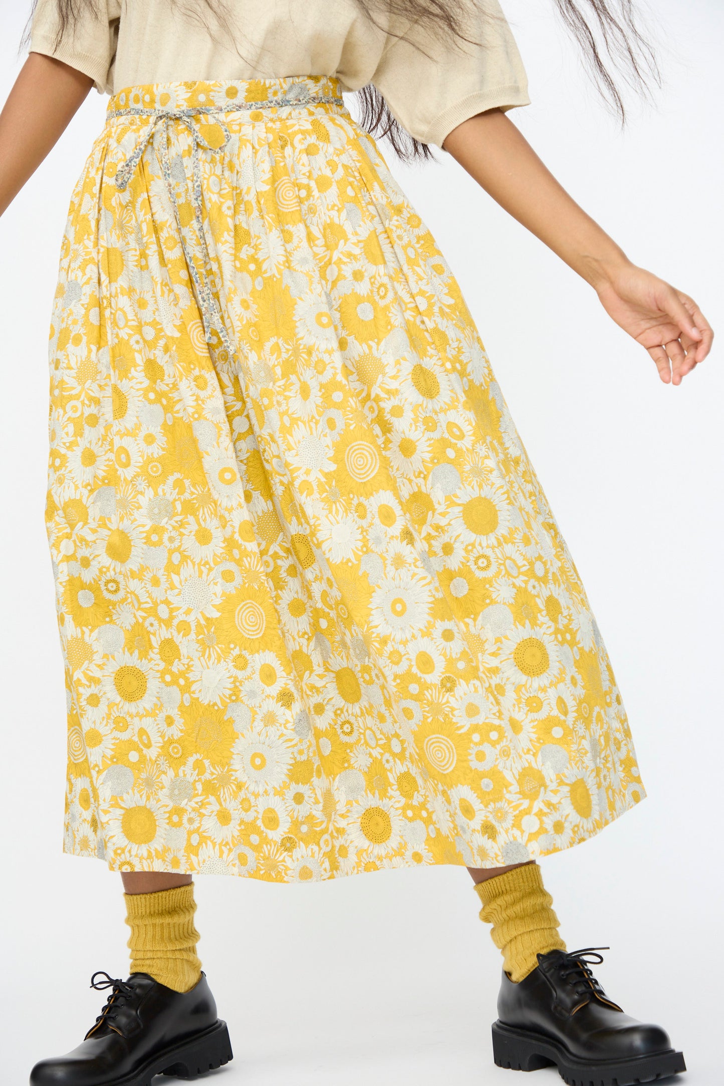 A person wearing a beige top, Ichi Antiquités Cotton Liberty Skirt in Yellow, mustard yellow socks, and black lace-up shoes stands against a white background.