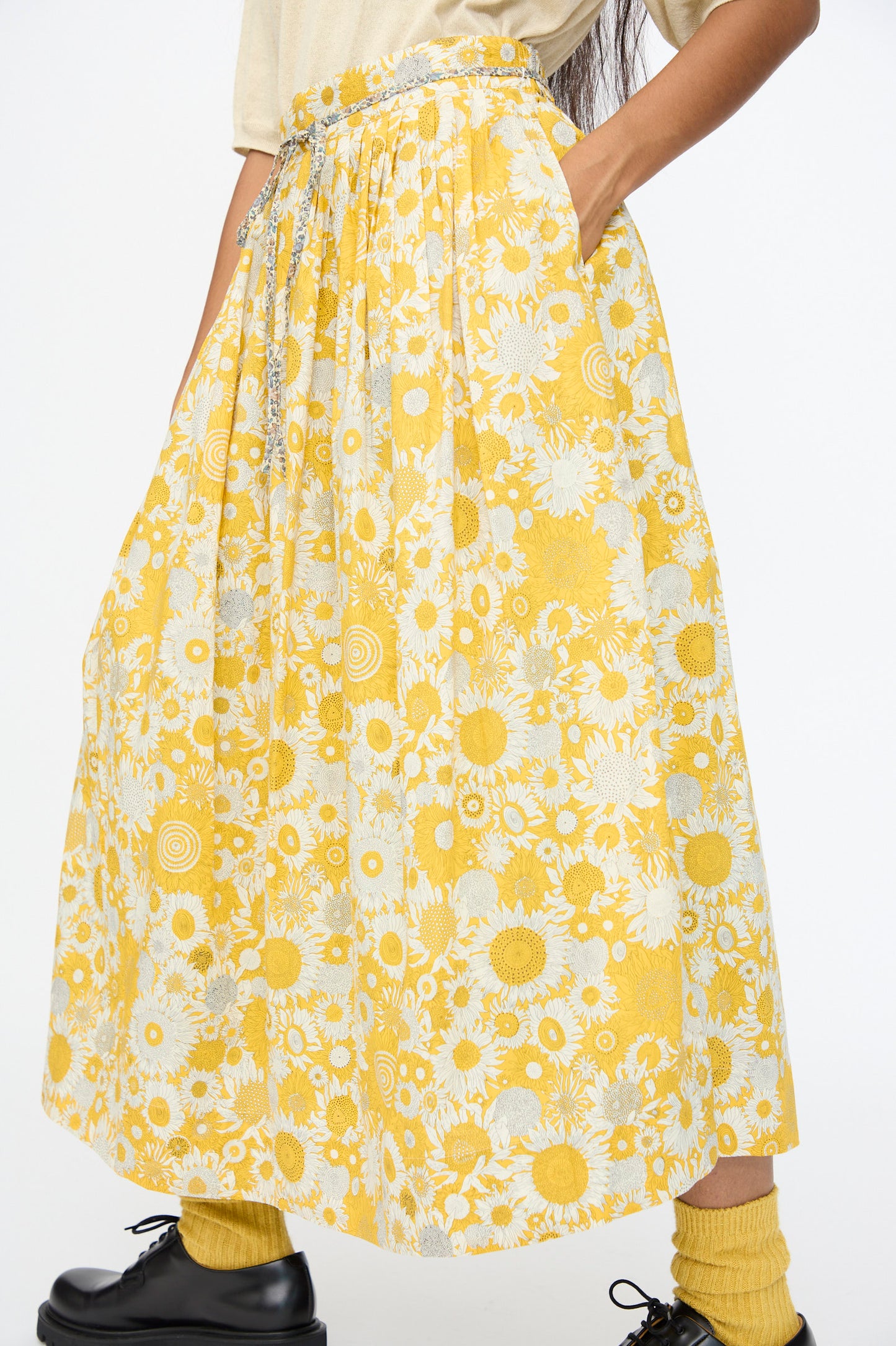 Someone wears the Ichi Antiquités Cotton Liberty Skirt in Yellow, paired with a beige top, yellow socks, black shoes, and has their hands in the skirt pockets.