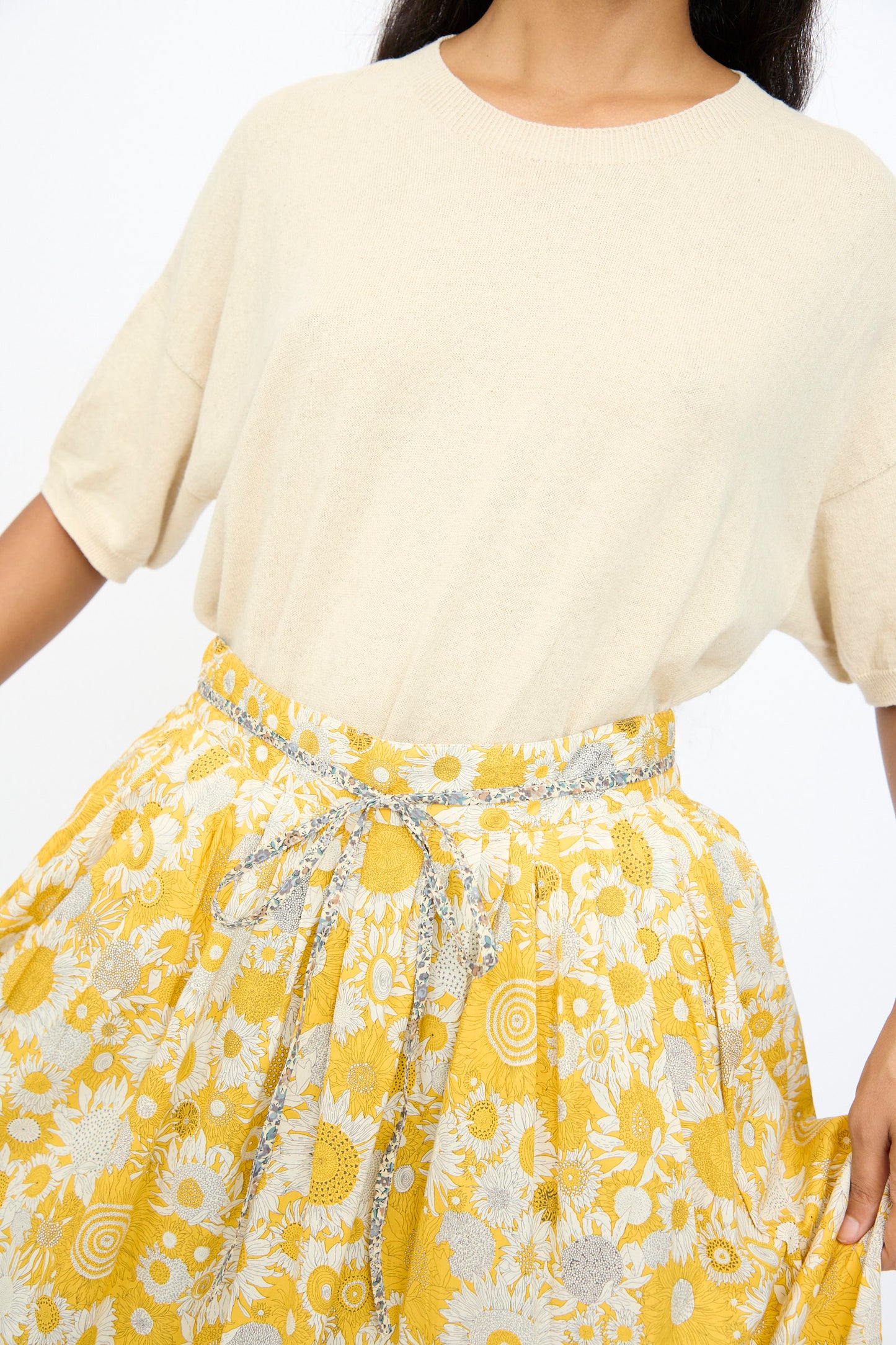 A person wearing a short-sleeved beige top paired with the Ichi Antiquités Cotton Liberty Skirt in Yellow, featuring a floral midi design and matching fabric belt.