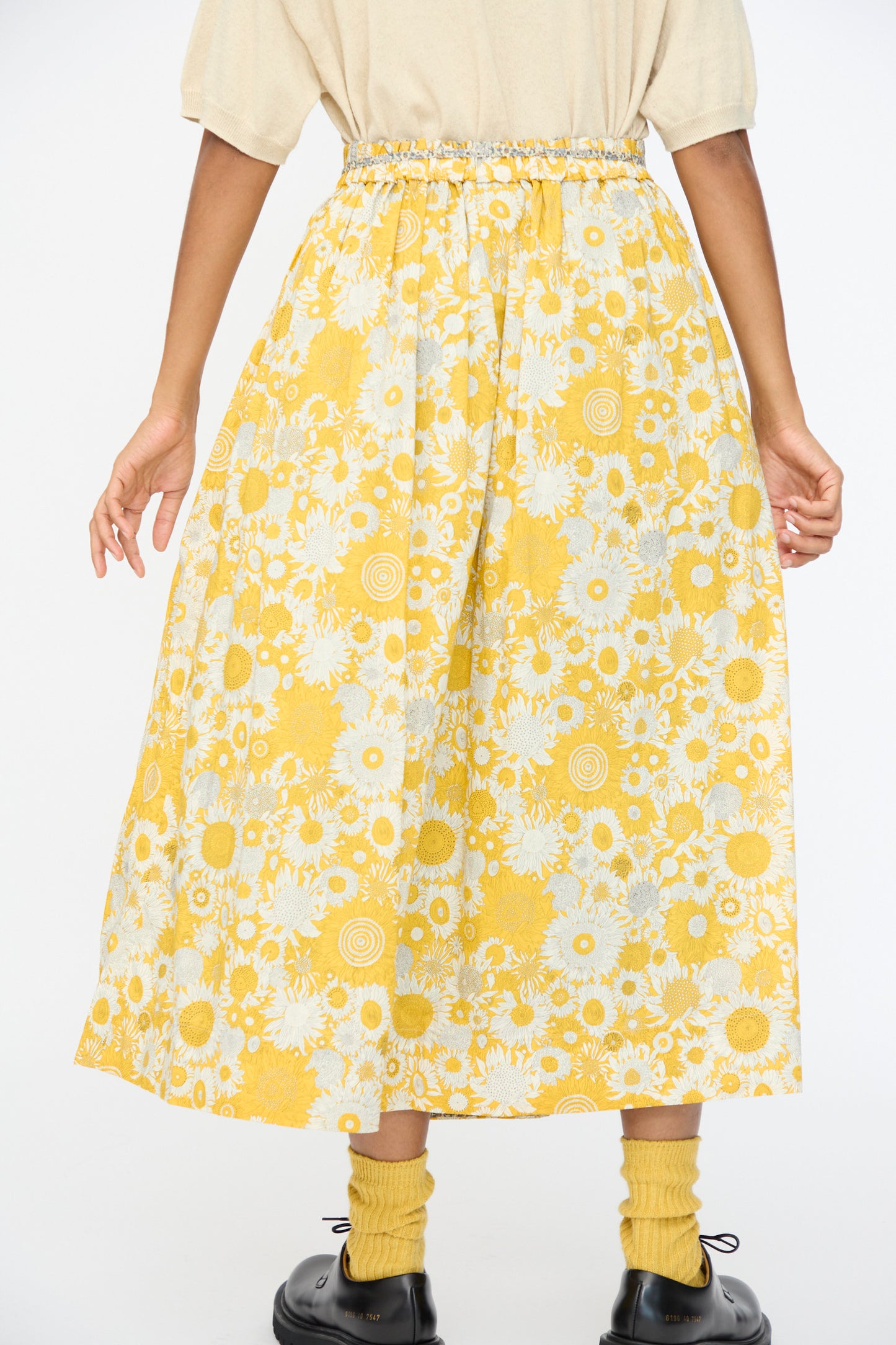 A person is shown from the back wearing a beige top and the Cotton Liberty Skirt in Yellow by Ichi Antiquités, styled with yellow socks and black shoes, against a plain white background.