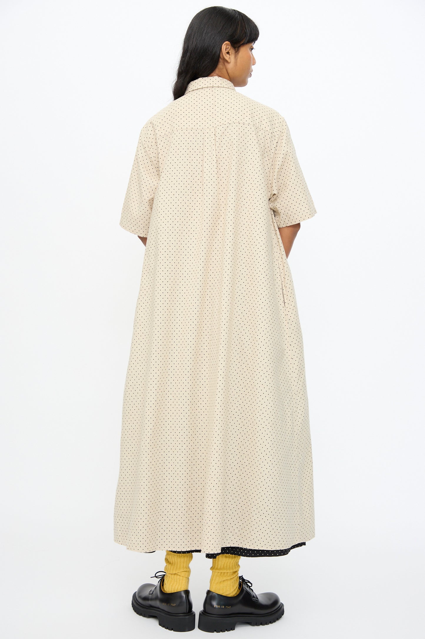 A person stands facing away, wearing the Ichi Antiquités Cotton Linen Dot Dress in Natural, styled with yellow socks and black shoes.